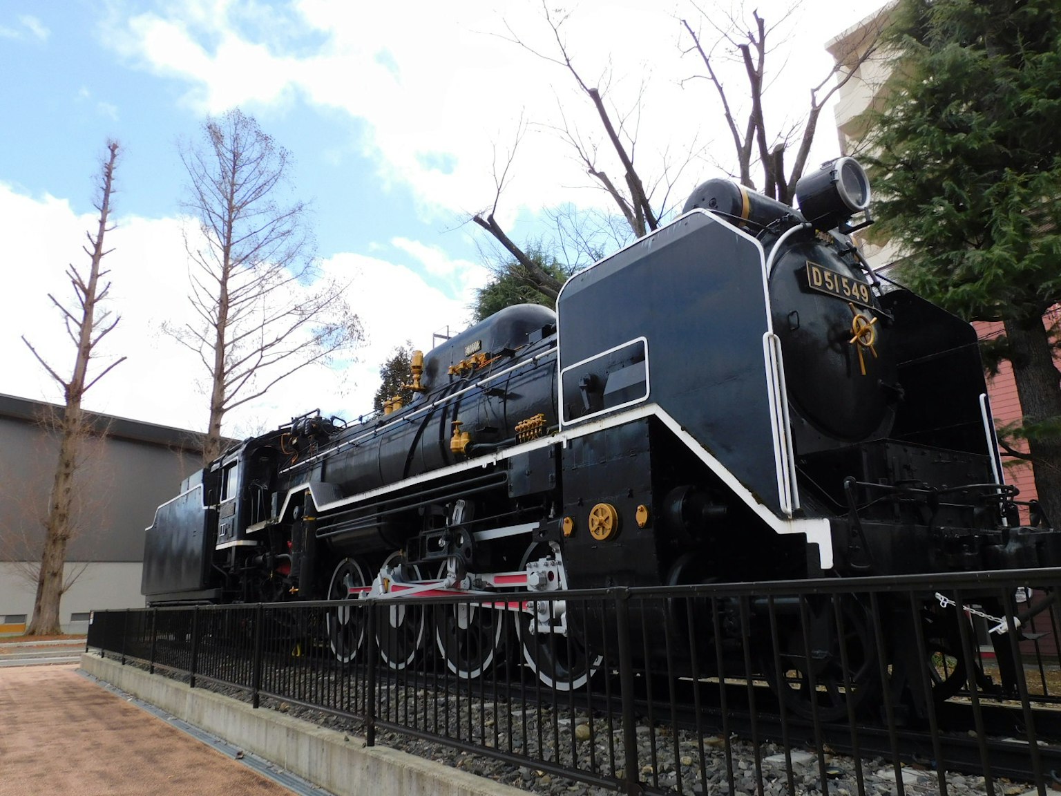 Side view of a black steam locomotive with blue sky and trees in the background