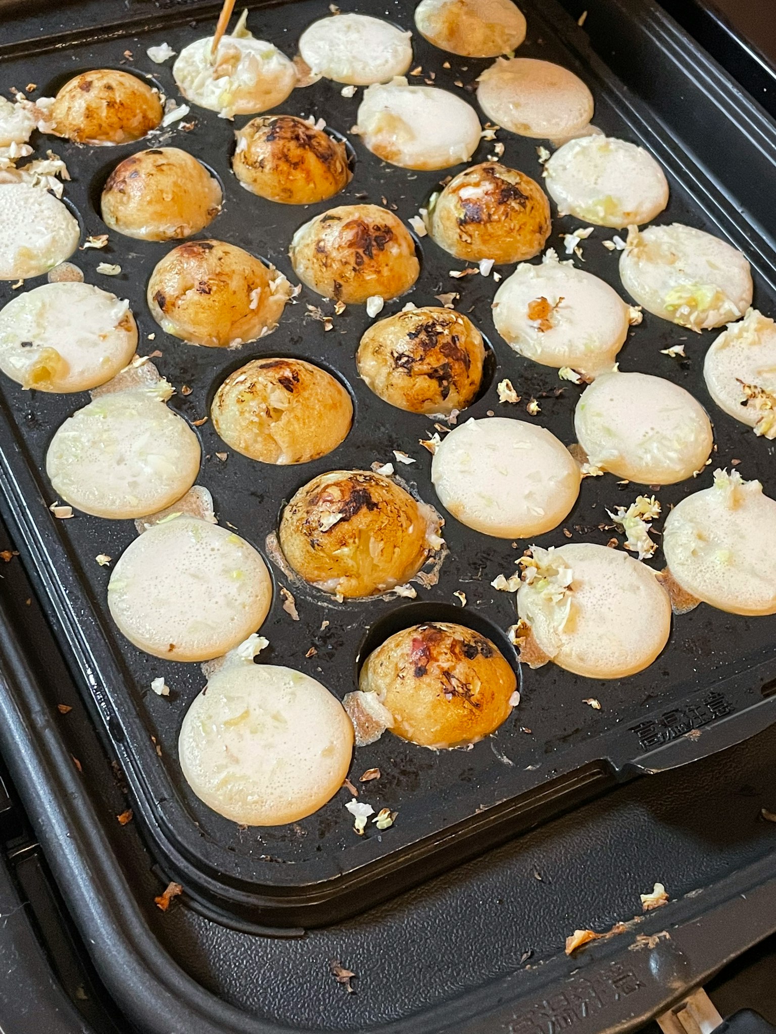 Takoyaki che cuoce su una piastra per takoyaki con sopra dorato