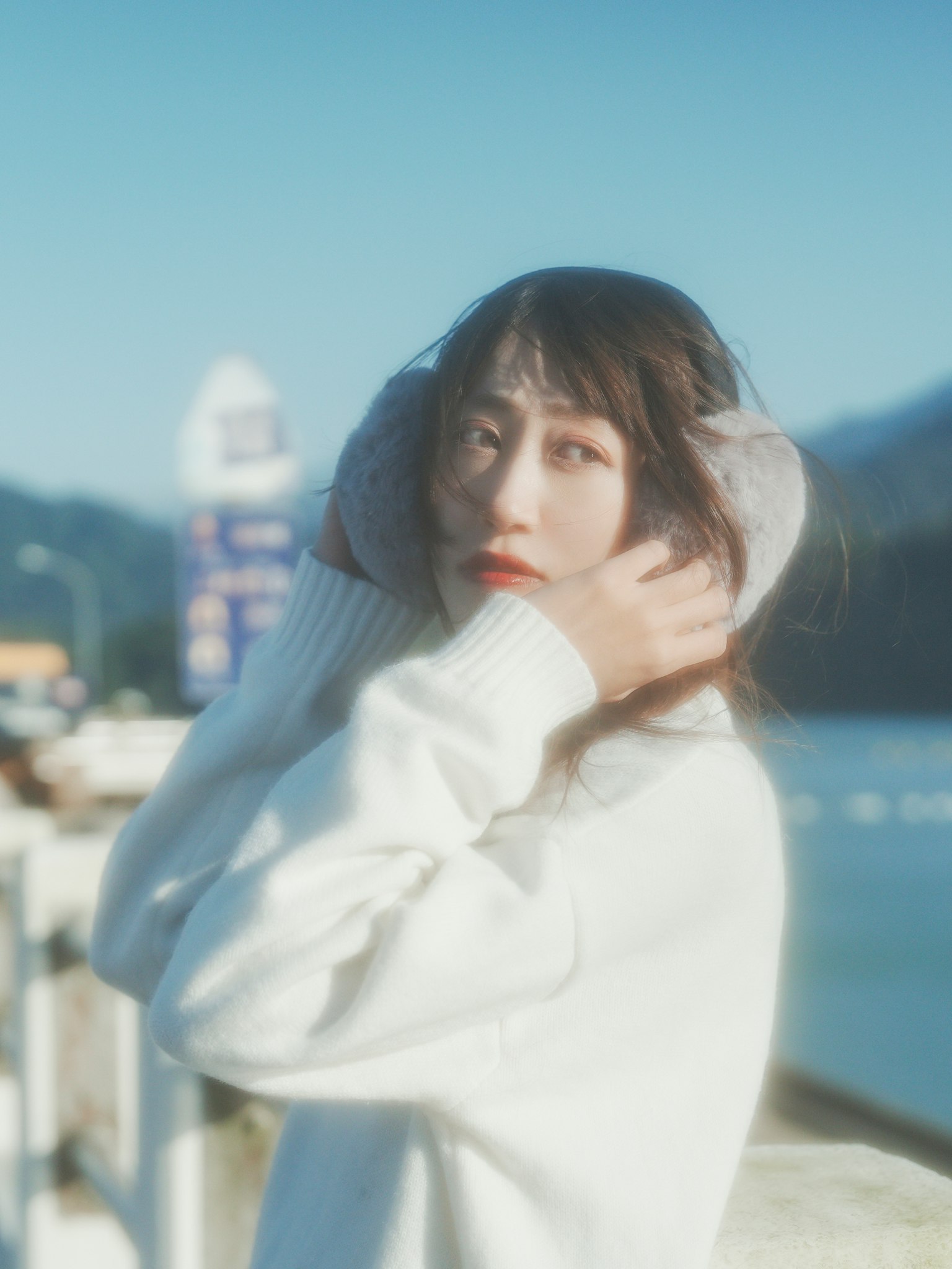 女性が白いセーターを着て耳を覆いながら微笑んでいる風景