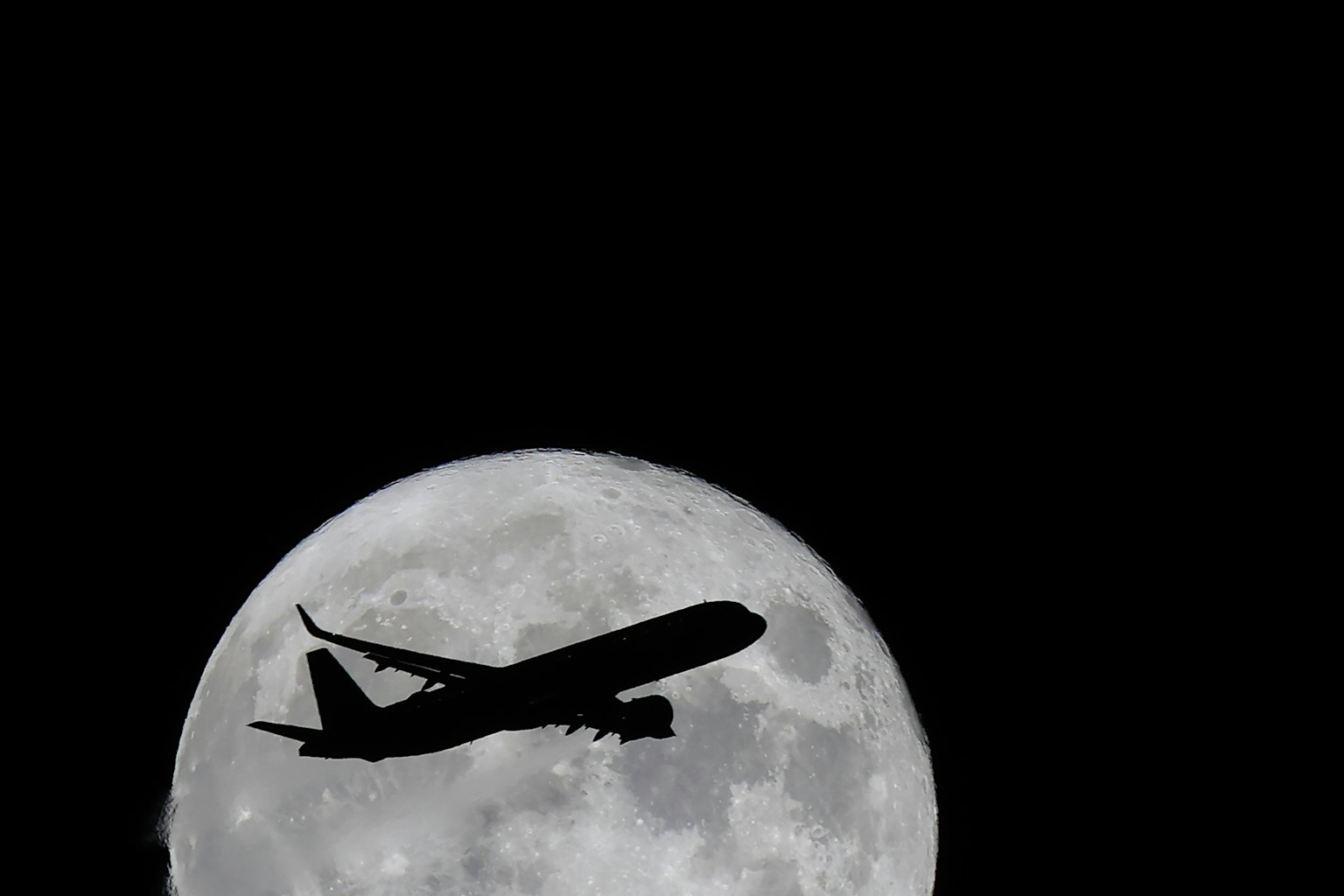 Silhouette eines Flugzeugs, das vor einem Vollmond fliegt
