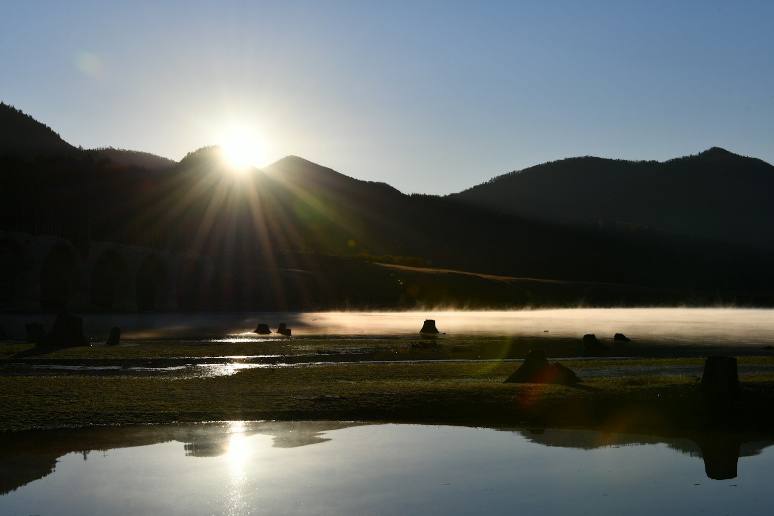Lever de soleil sur un lac brumeux avec des montagnes en arrière-plan