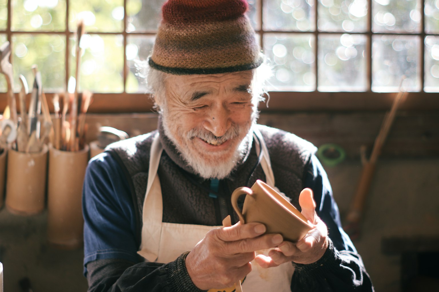 Smiling elderly craftsman holding a pottery mug in a workshop setting
