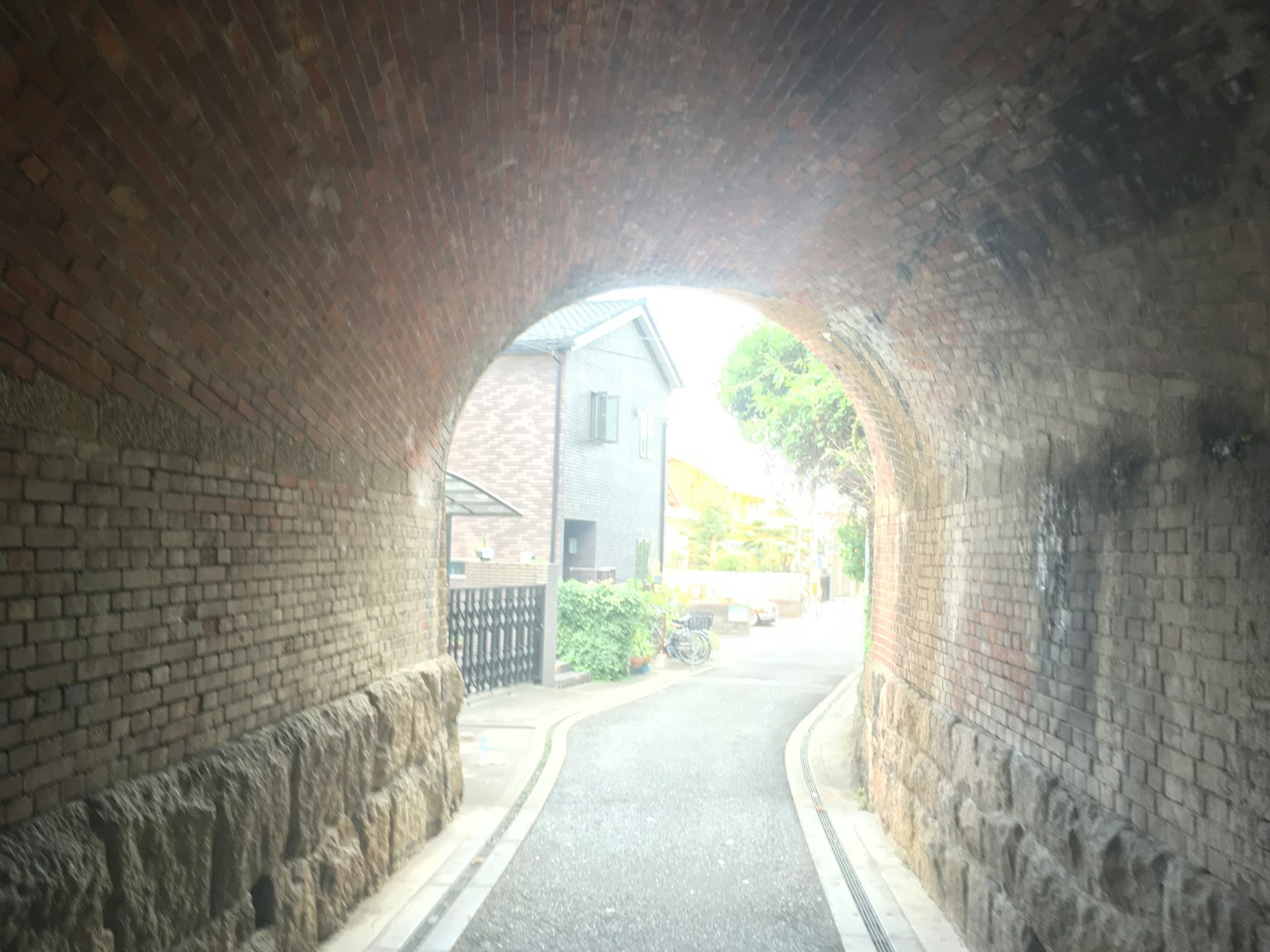Ziegelsteinbogen-Tunnel, der zu einer ruhigen Straße und Häusern führt