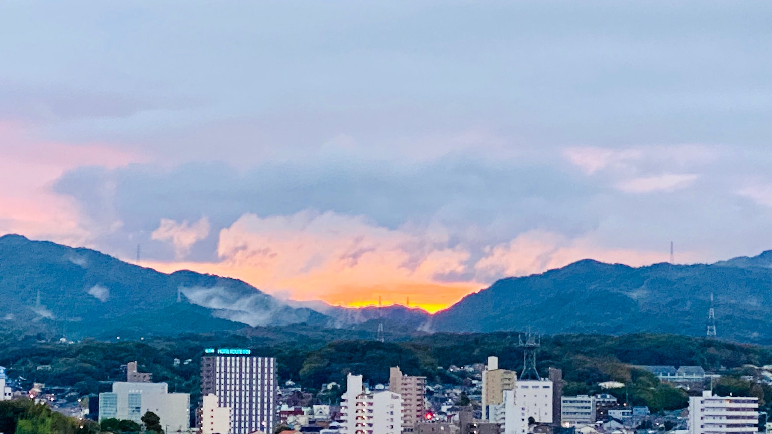 ท้องฟ้ายามพระอาทิตย์ตกเหนือทิวทัศน์เมืองที่มีภูเขาเป็นพื้นหลัง
