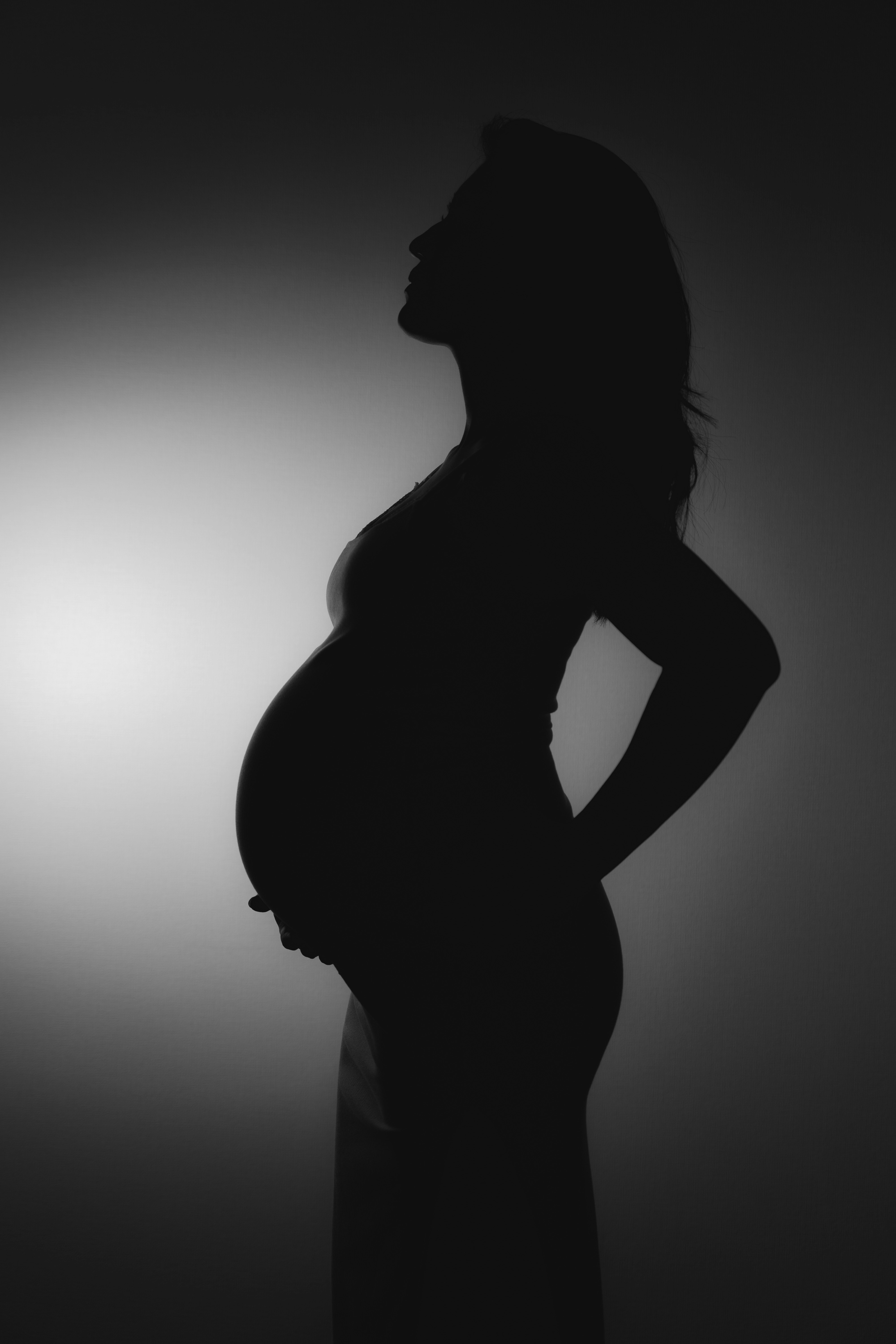 シルエットの妊婦が横向きに立つモノクロのポートレート