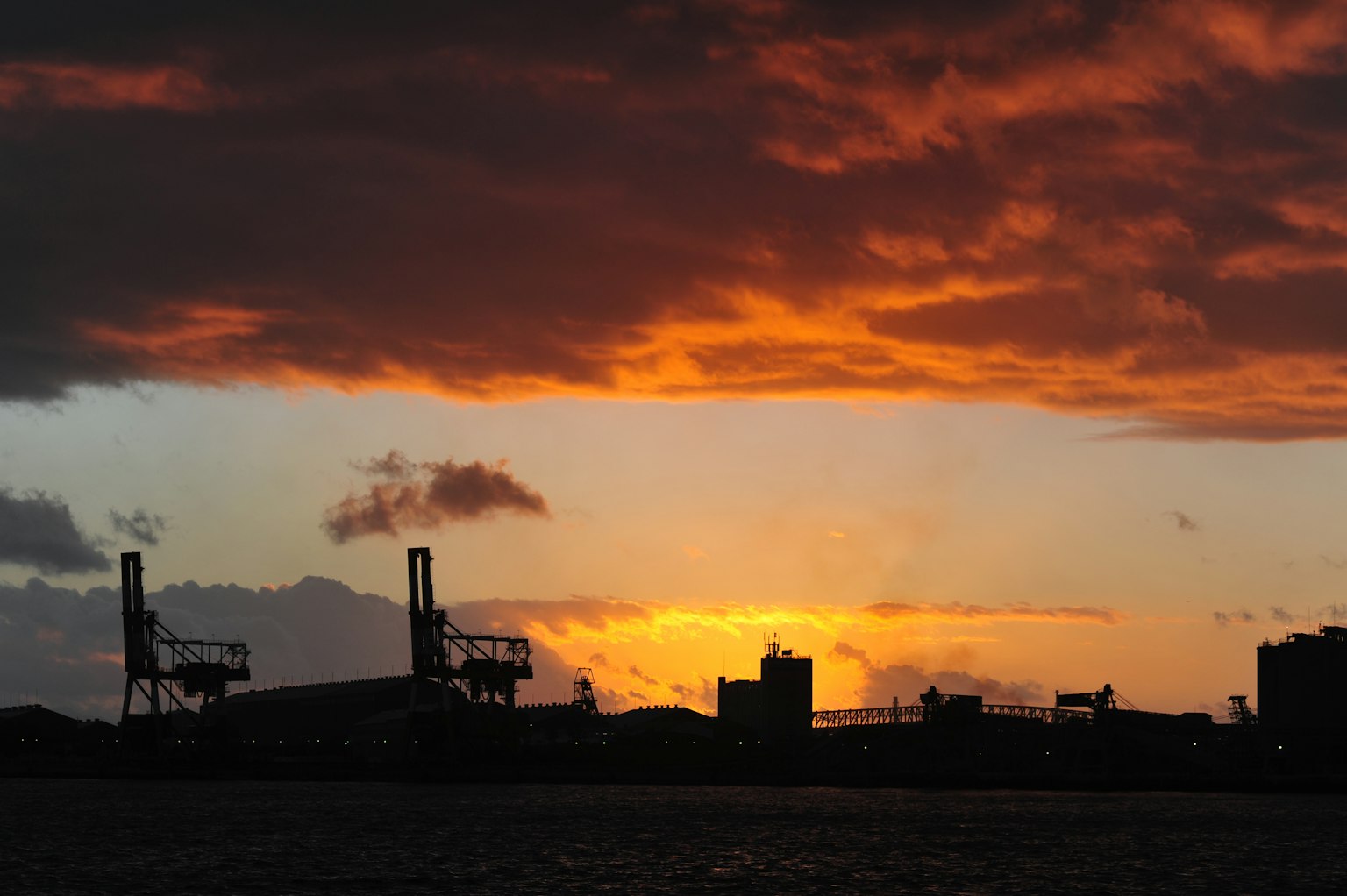 Silhouette eines Hafens mit Kränen vor einem lebhaften Sonnenuntergang