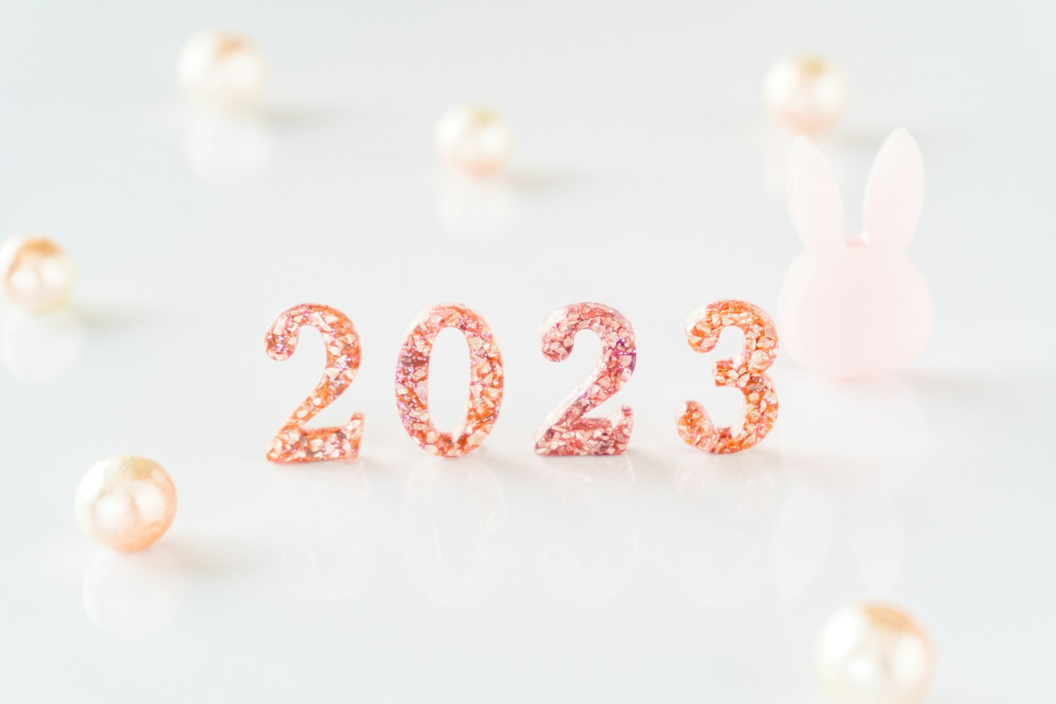 一個簡單的設計，特寫閃亮的粉色數字2023，周圍環繞著柔和的珍珠