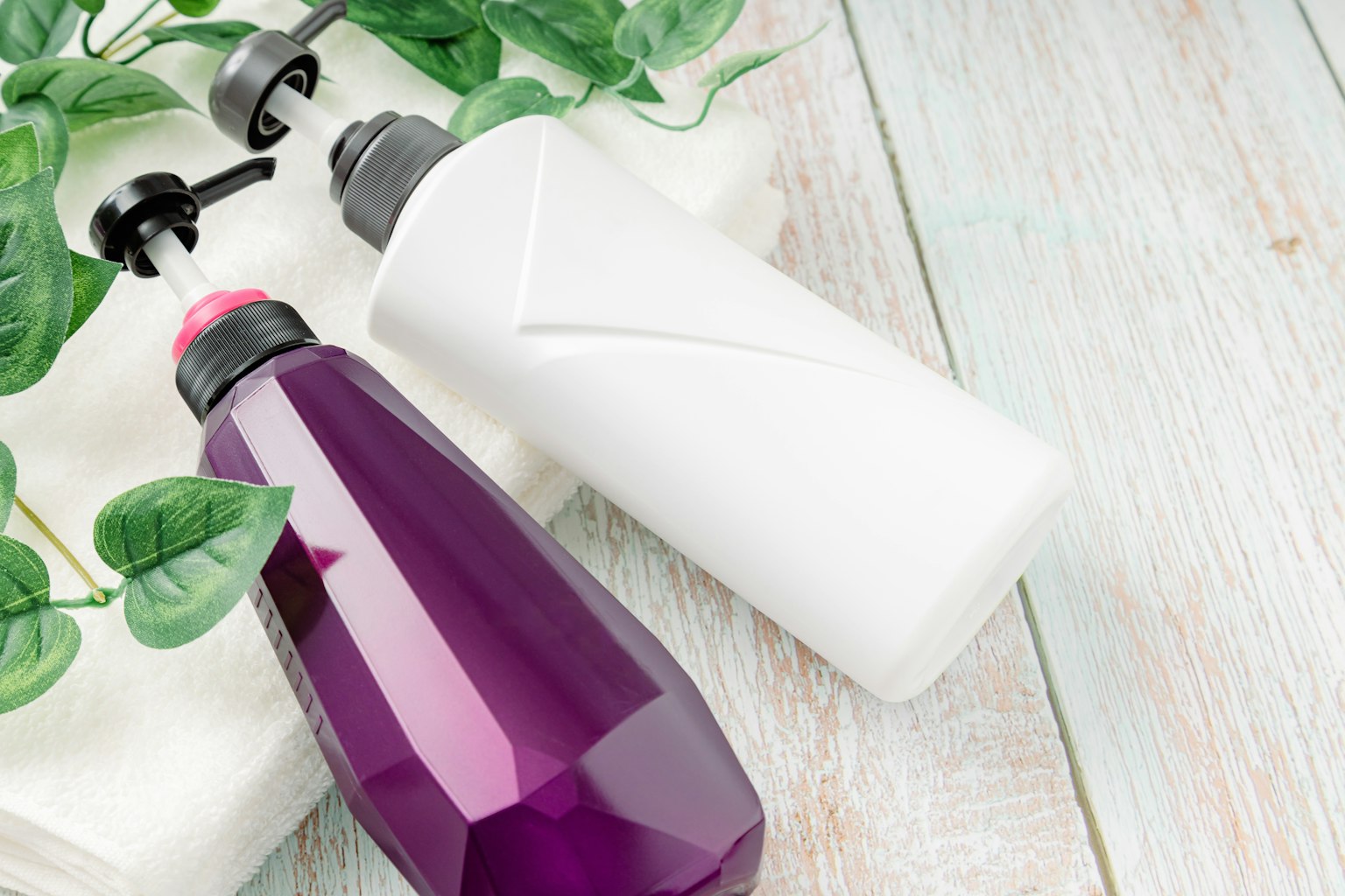Dua botol satu ungu dan satu putih diletakkan di atas permukaan kayu ringan dikelilingi oleh daun hijau