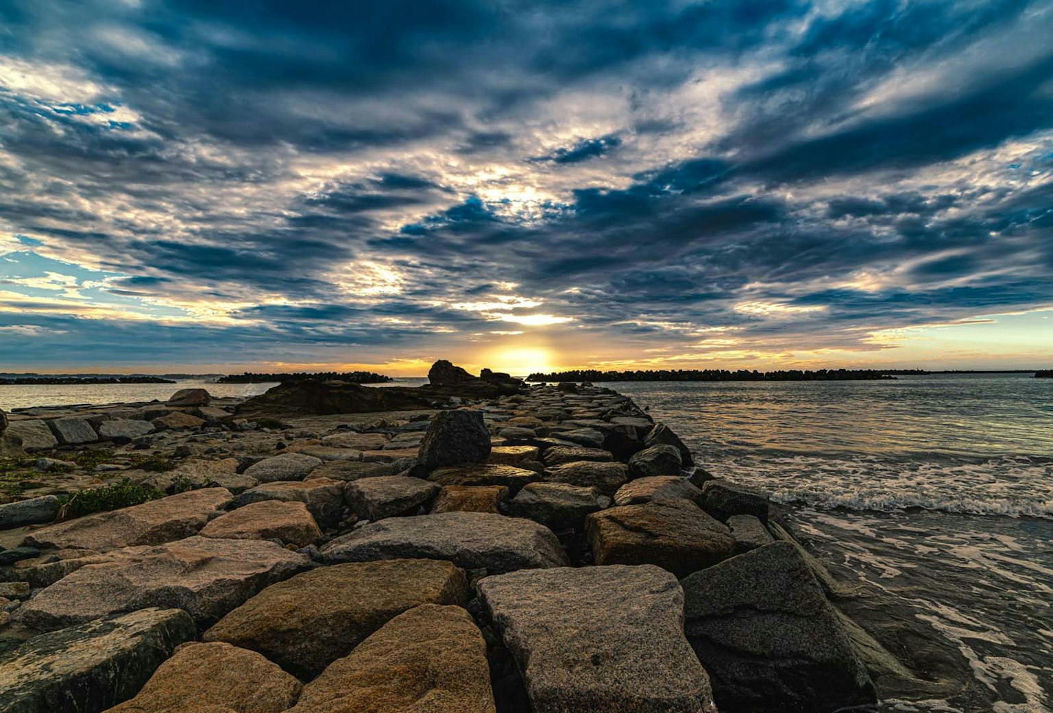 Muelle rocoso al atardecer con nubes dramáticas y agua tranquila