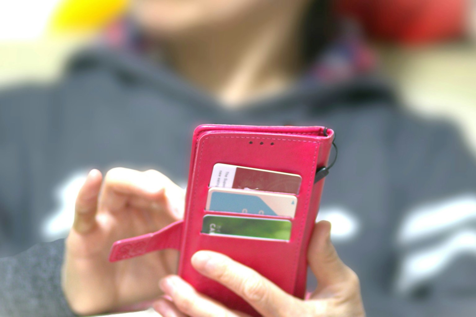 Main tenant un étui de smartphone rose vif avec des cartes visibles à l'intérieur et une personne floue en arrière-plan