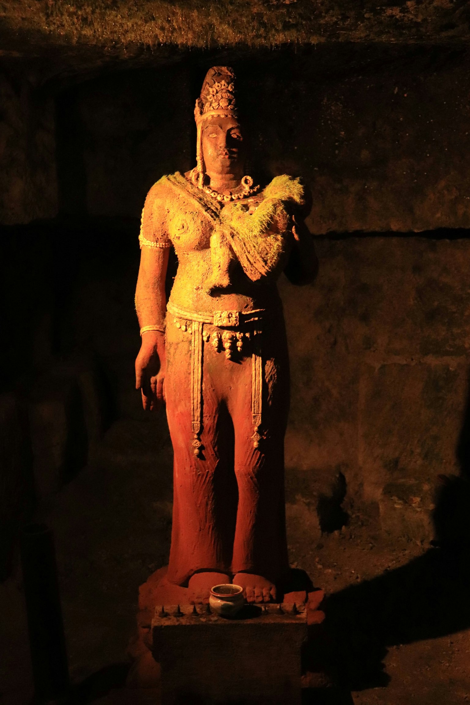 Ancient statue standing in a cave with vibrant decorations and attire