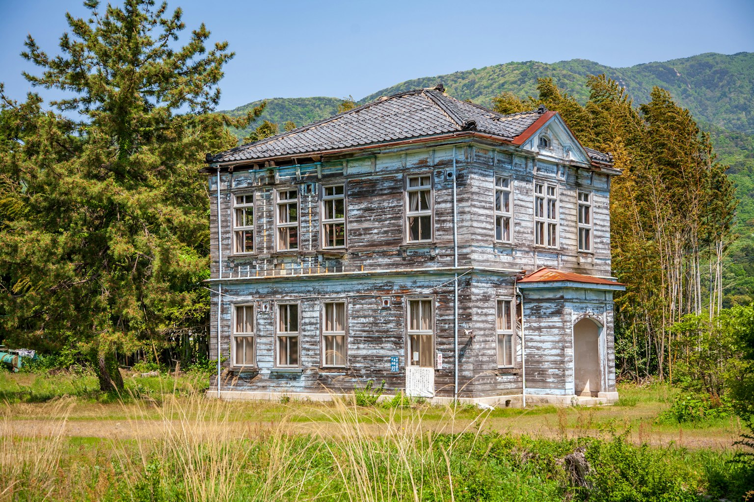 Un vecchio edificio in legno con vernice blu scrostata circondato da vegetazione