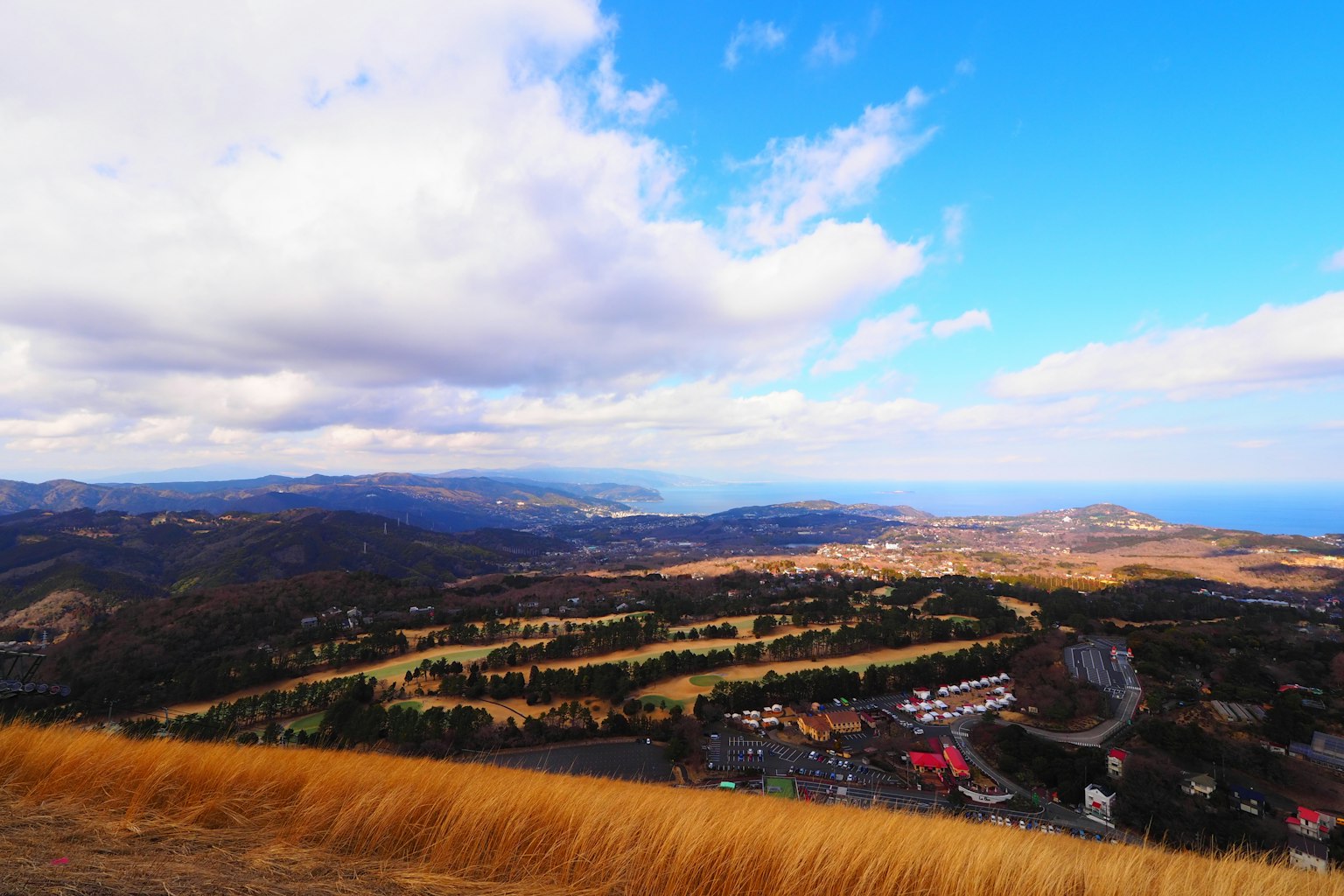 Vista escénica de montañas bajo un cielo azul con nubes océano distante visible campos verdes y área residencial abajo