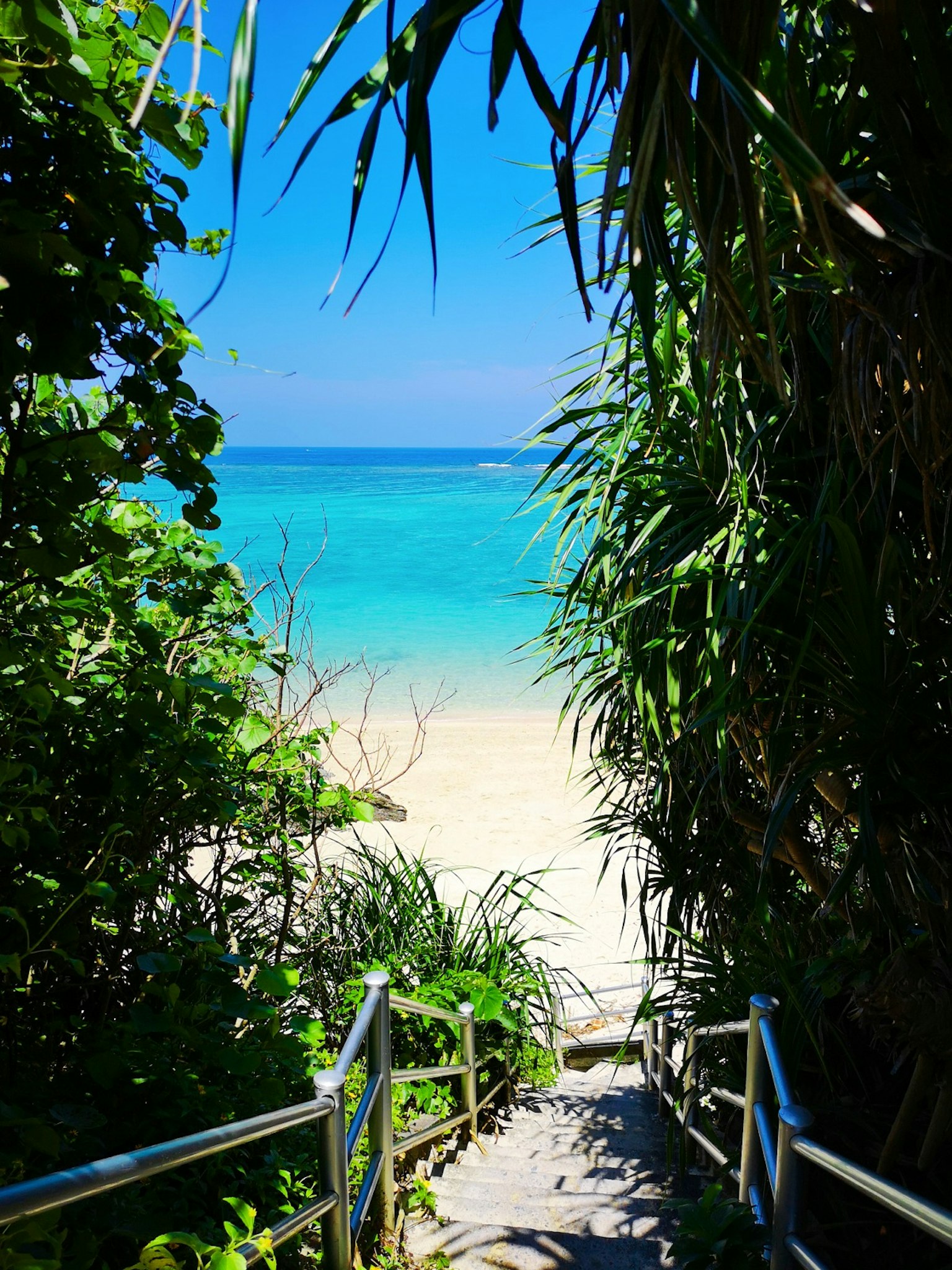 Tangga yang menuju pantai dengan air turquoise dan pasir putih