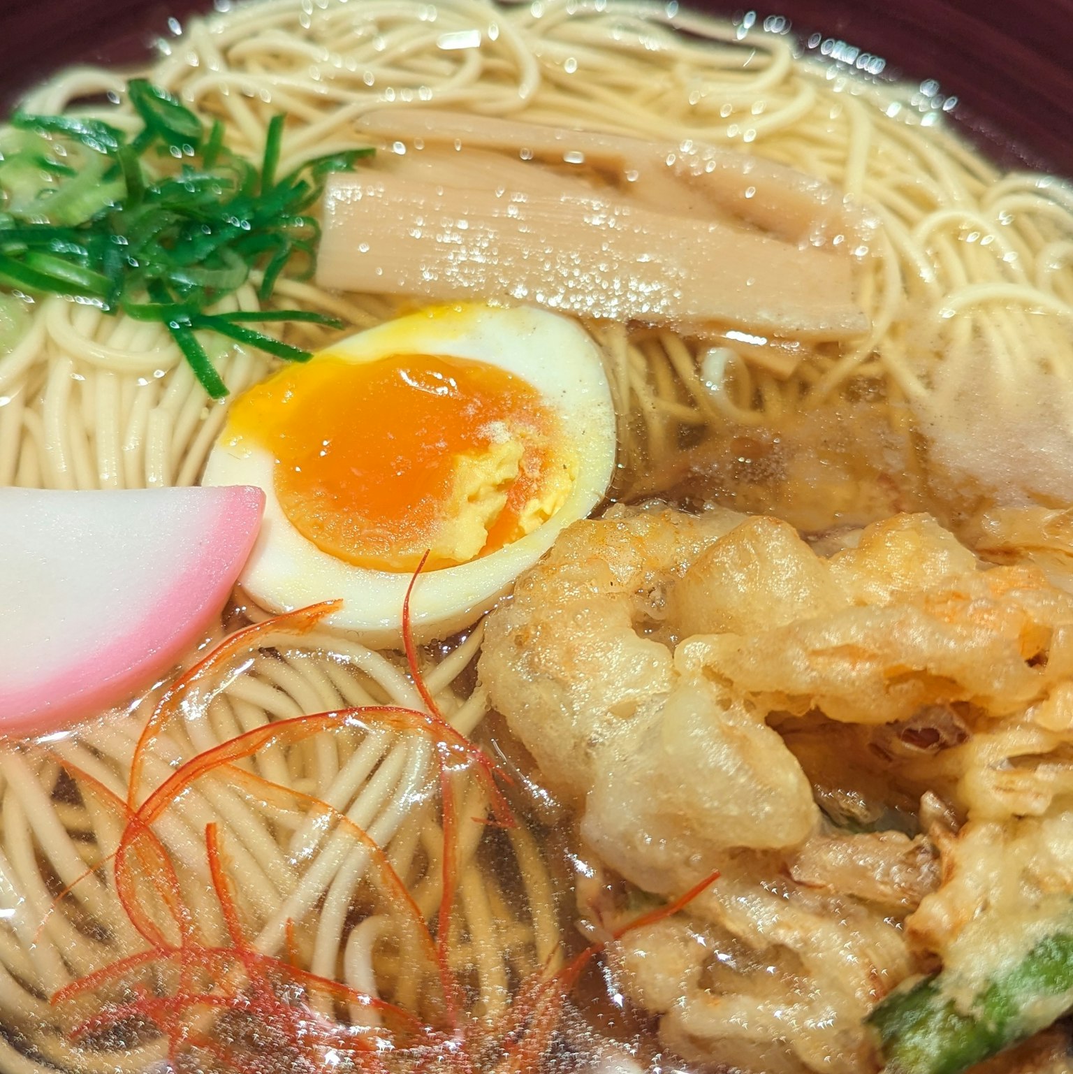 一碗美味的拉麵，上面放著半熟蛋、天婦羅、青蔥、筍乾和魚板