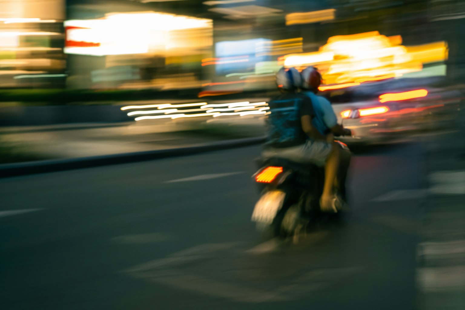 Immagine sfocata di un motociclista e di un passeggero che sfrecciano in una città di notte
