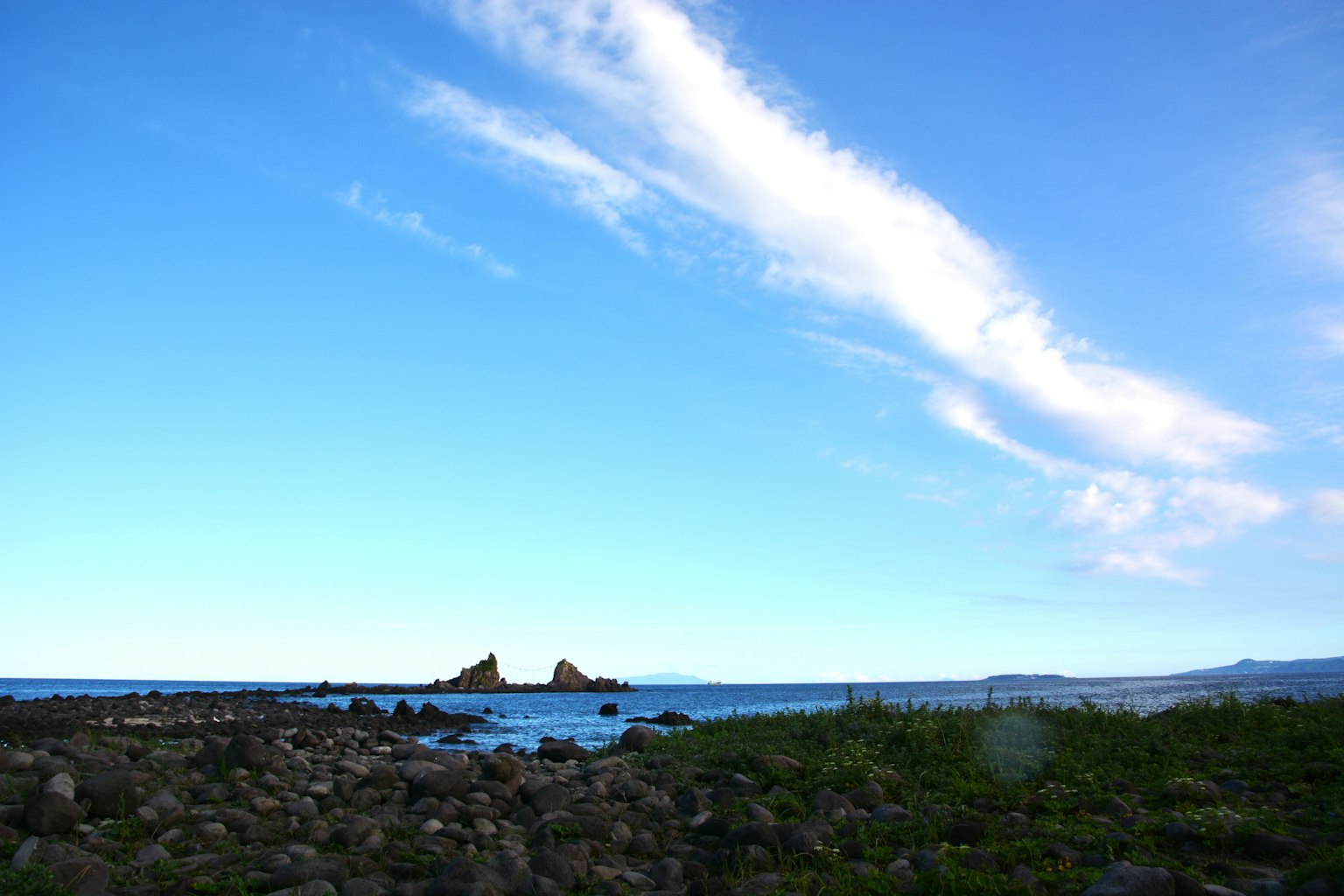 Pemandangan pantai dengan langit biru dan awan di tepi berbatu dan rumput hijau