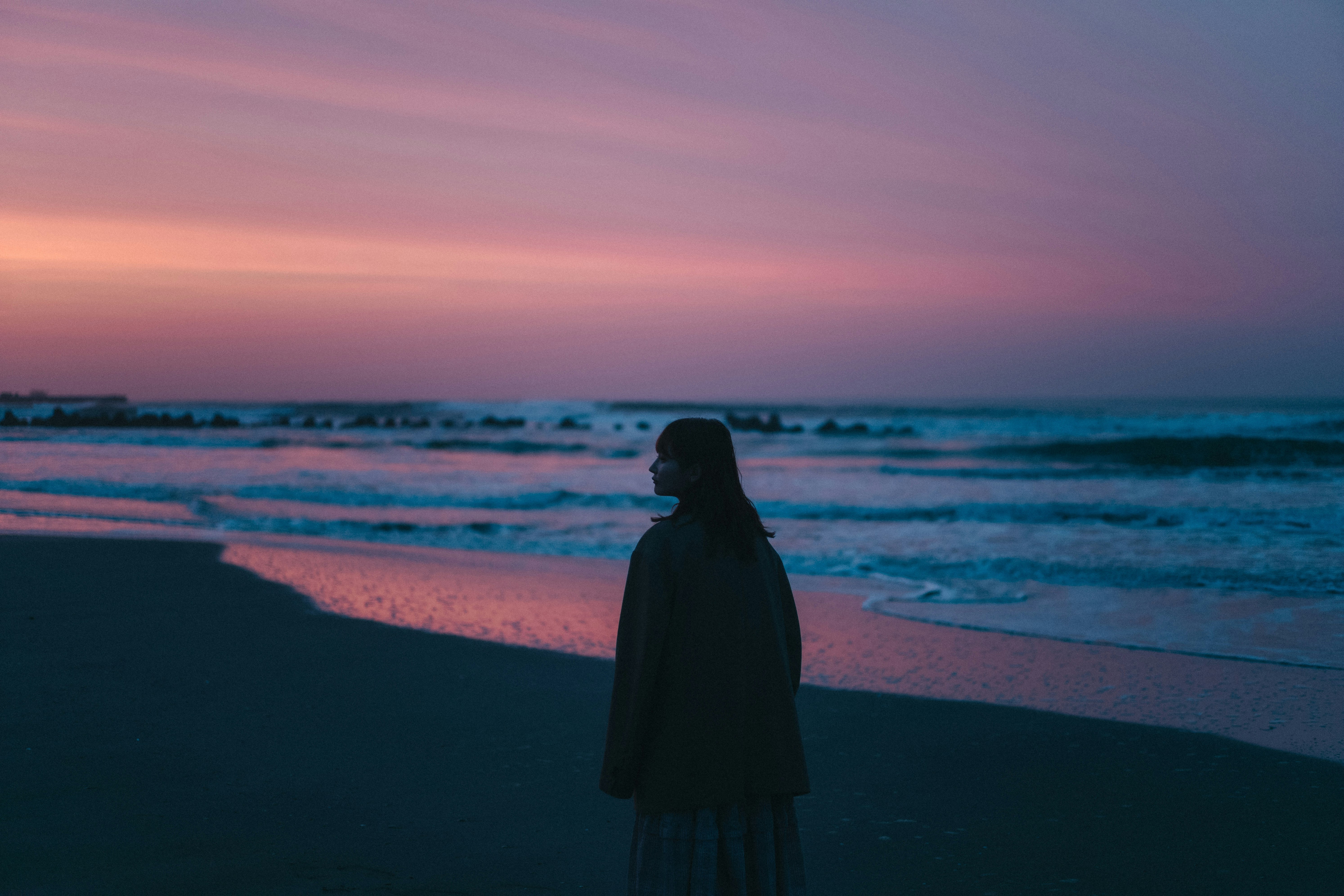 夕暮れの海辺で佇む人物のシルエット