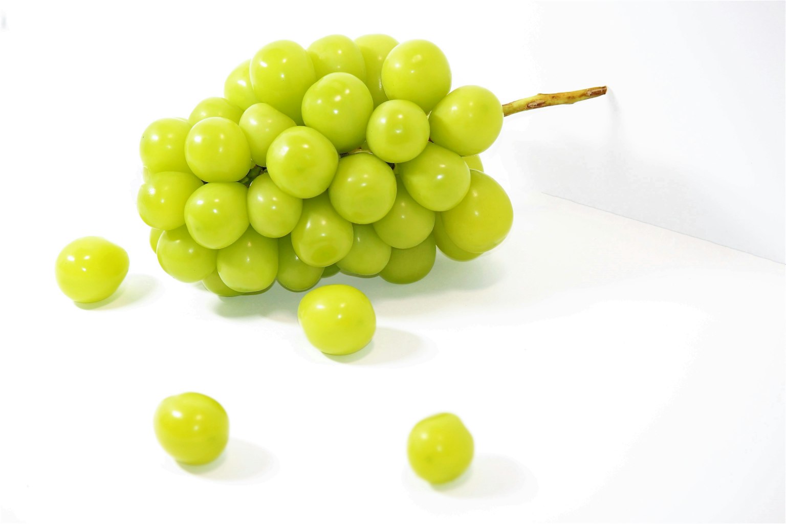 Grappes de raisins verts frais avec plusieurs raisins éparpillés sur un fond blanc