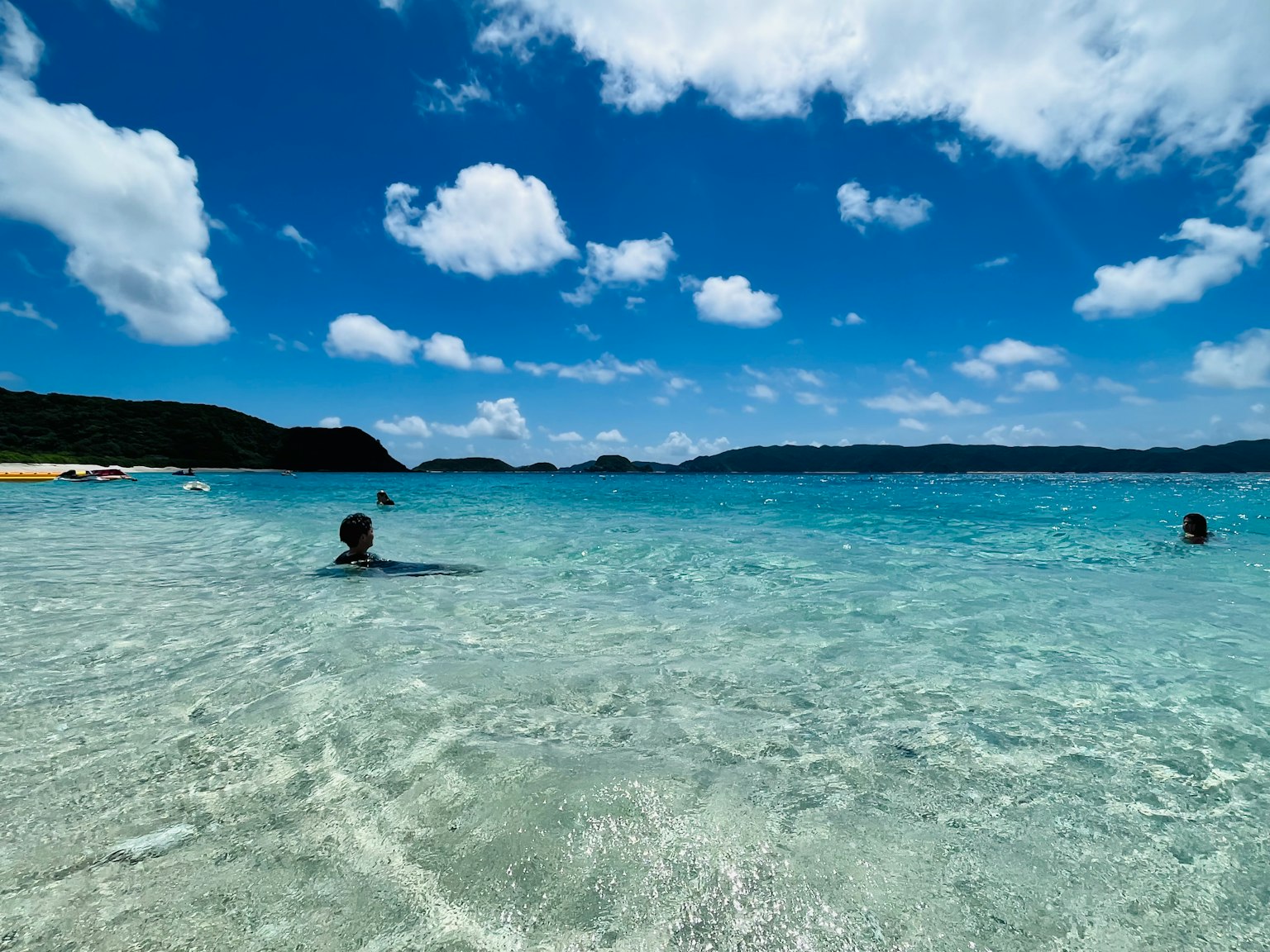 风景如画的海滩景观，人在清澈的蓝色水中游泳，阳光明媚