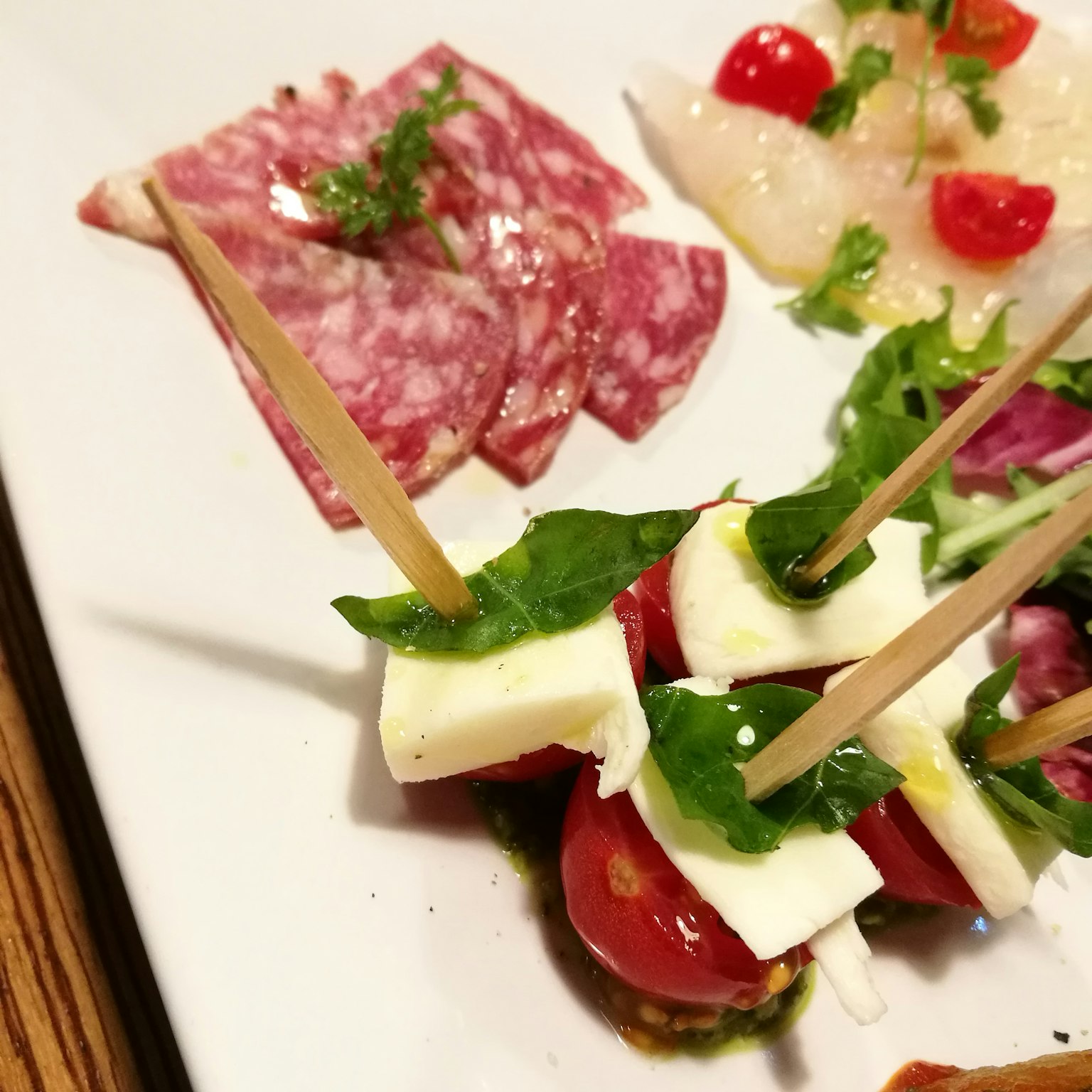 Piatto di antipasti colorato con salame, pesce, spiedini di pomodoro e mozzarella