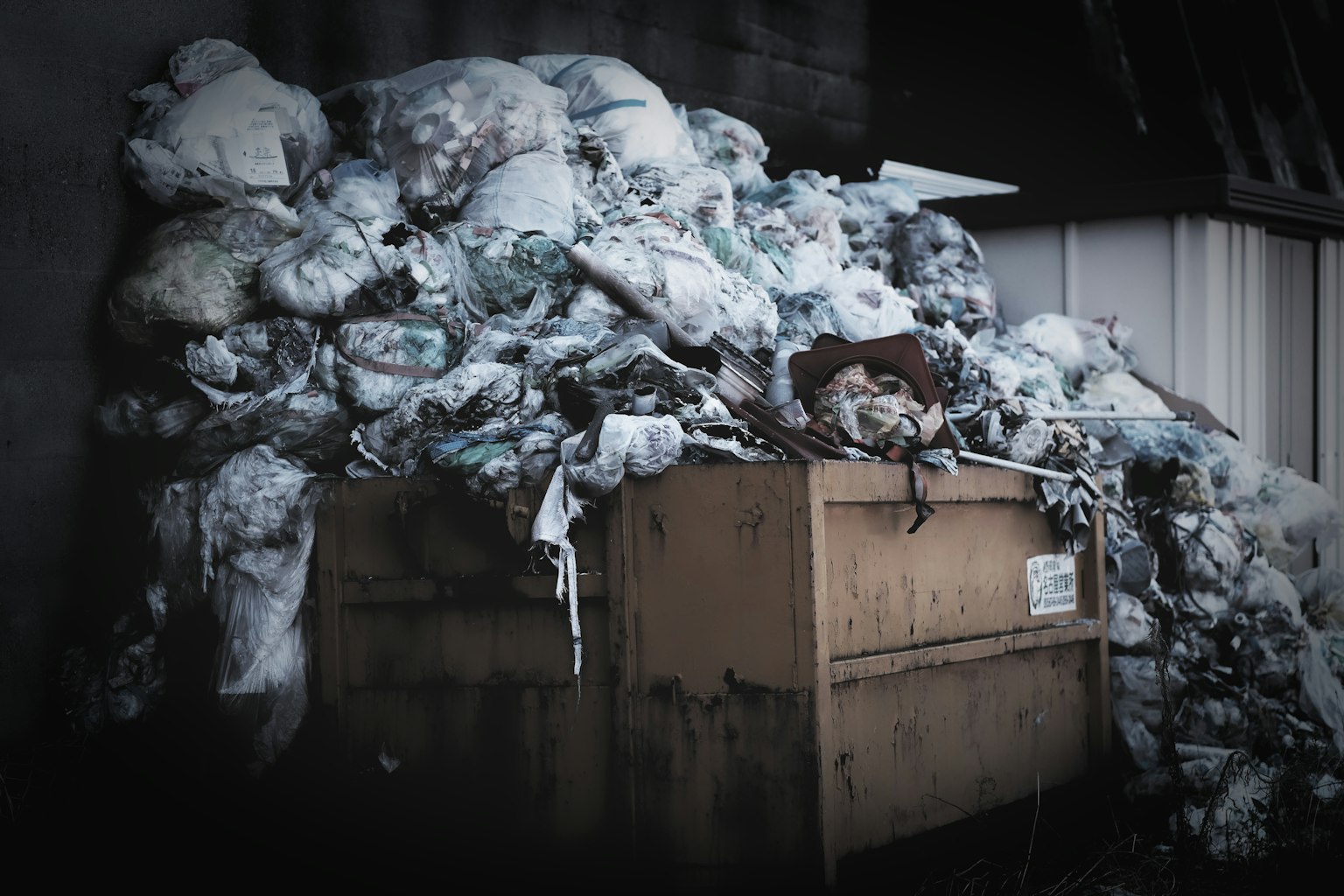Image of a dumpster overflowing with garbage bags