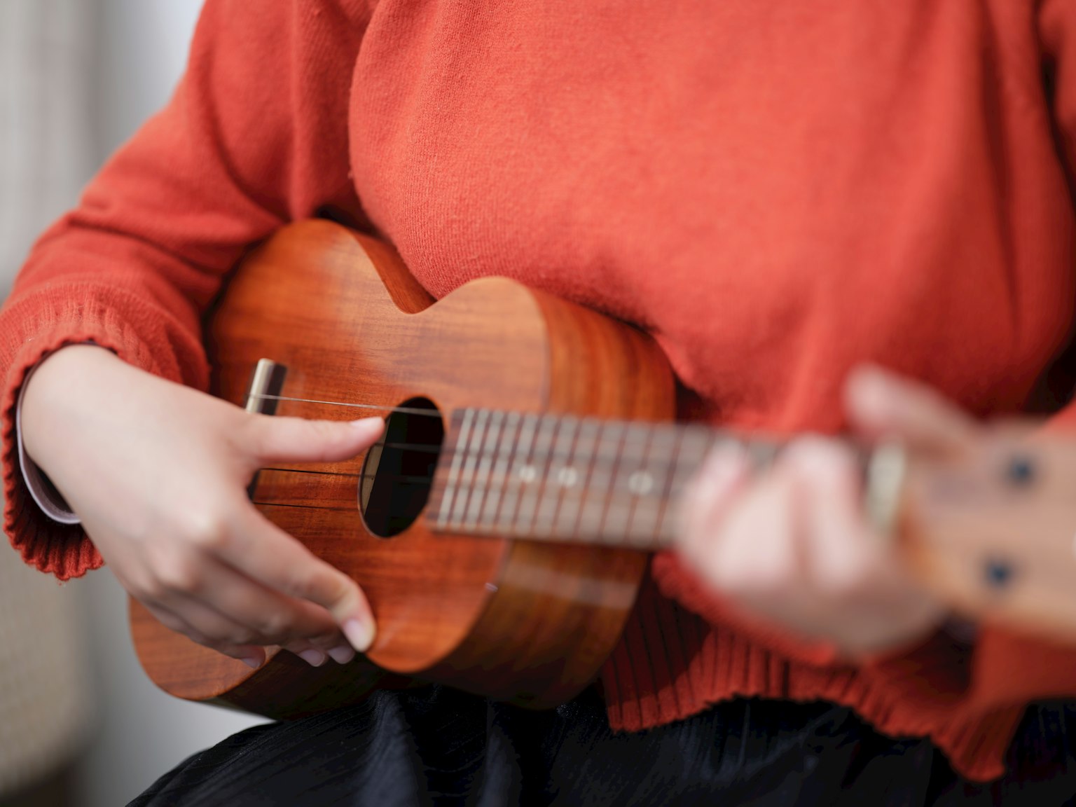 Wanita bermain ukulele mengenakan sweter oranye