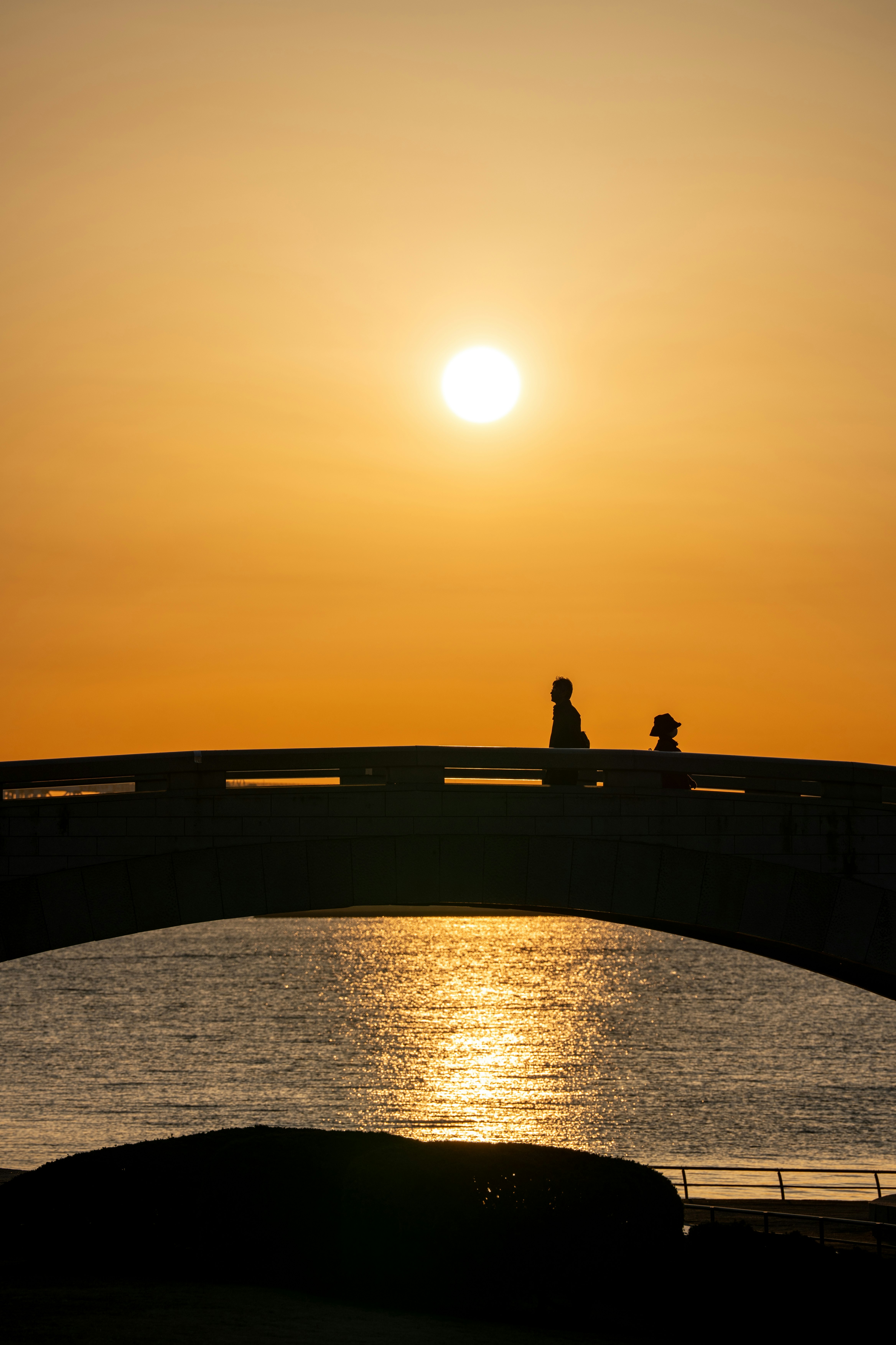 夕日に照らされた海沿いの橋の上で夕暮れを眺める人