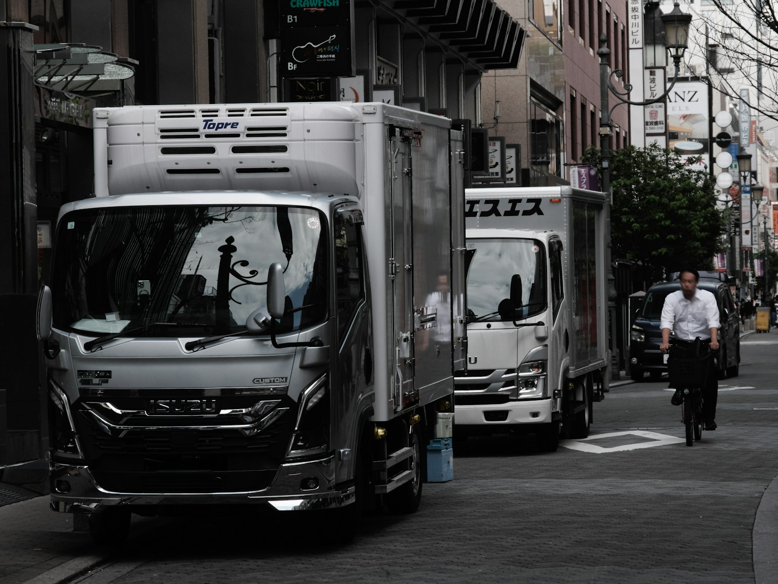 Silver trucks parked in a narrow street with a man riding a bicycle