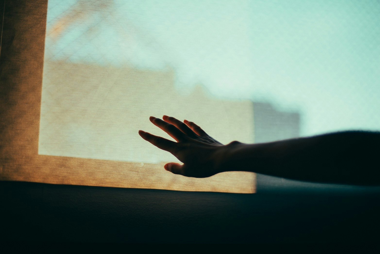 quiet indoor scene with a hand reaching toward the light by a window