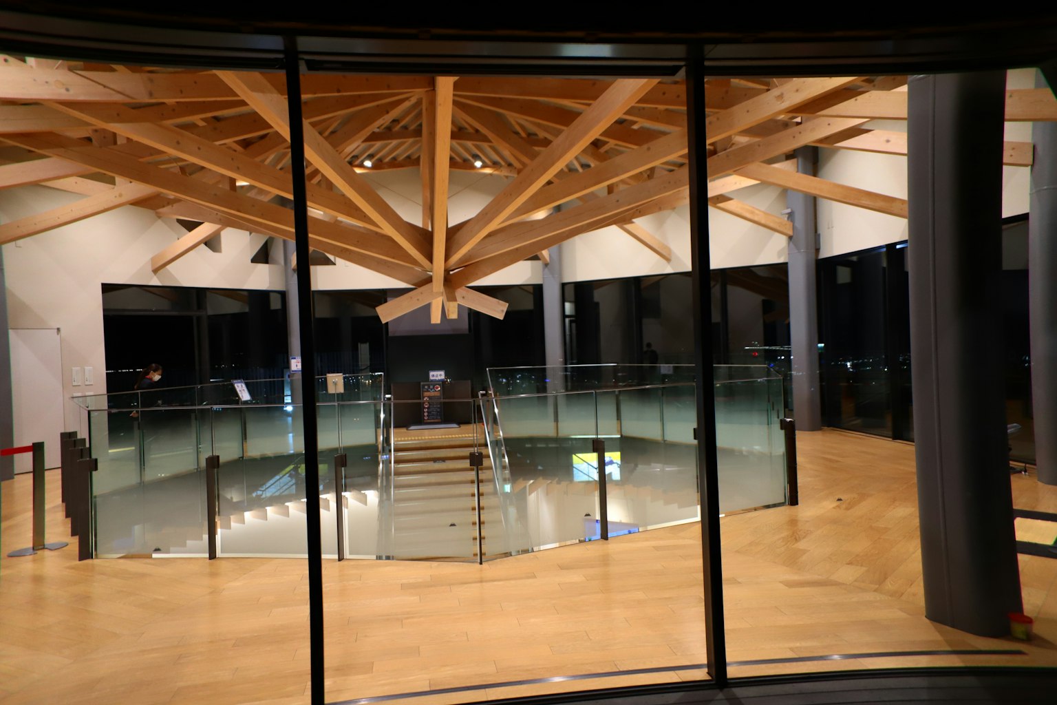 Intérieur d'un bâtiment moderne avec des poutres en bois et des murs en verre, avec un escalier central