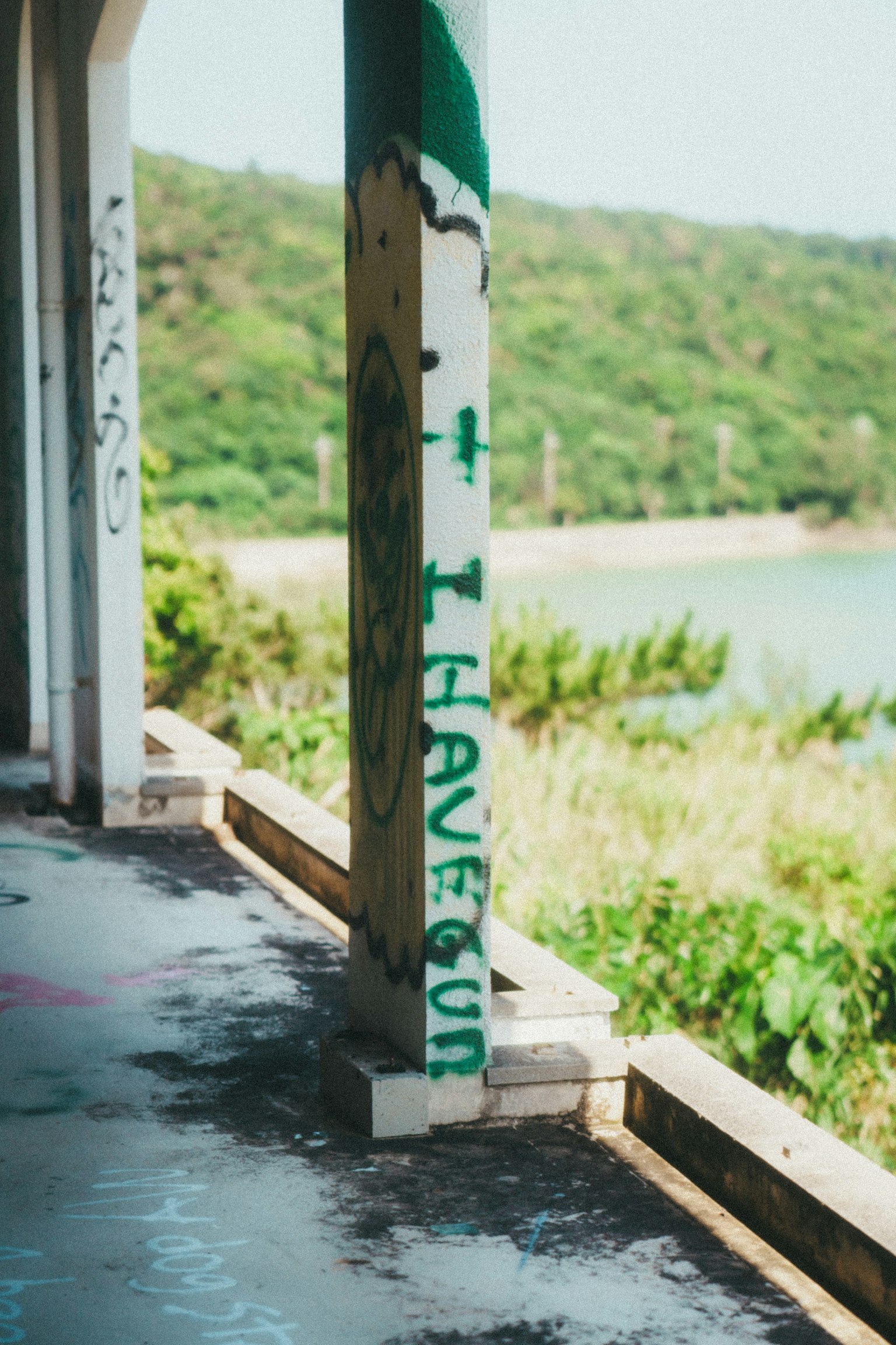 風化的柱子上的塗鴉，綠色文字，背景是綠色山丘和水