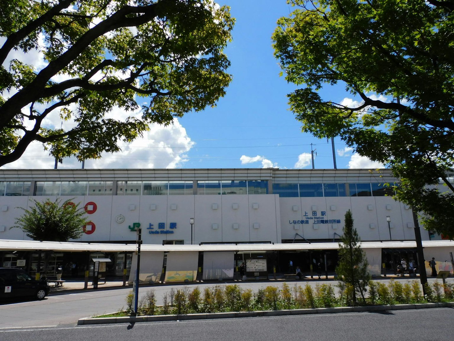 Vista exterior de una estación de tren con árboles y cielo azul