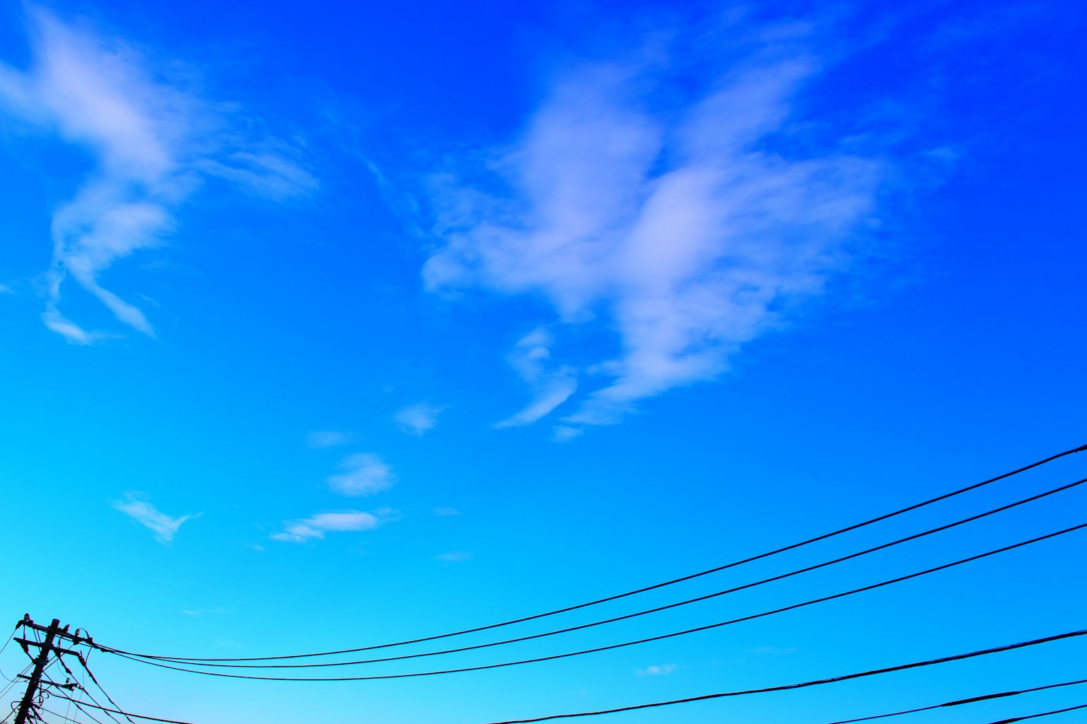 Ciel bleu vibrant avec des nuages blancs épars lignes électriques au bas de l'image