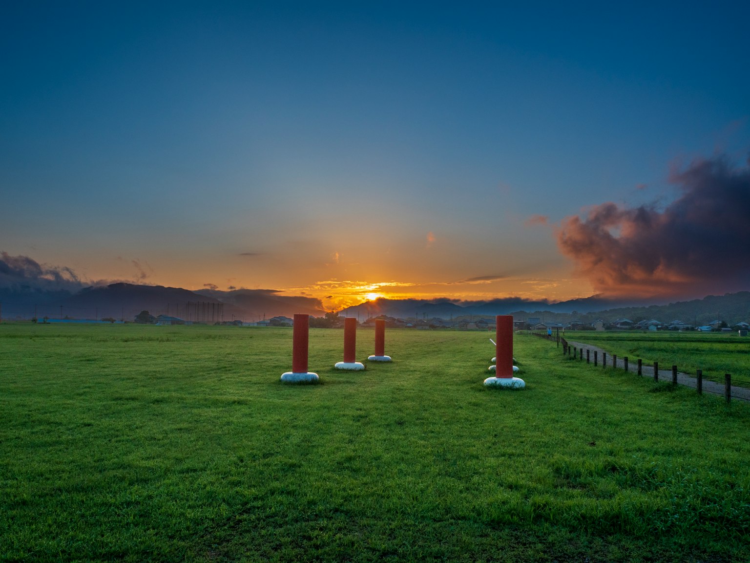 Rote Säulen in einem grünen Feld bei Sonnenuntergang