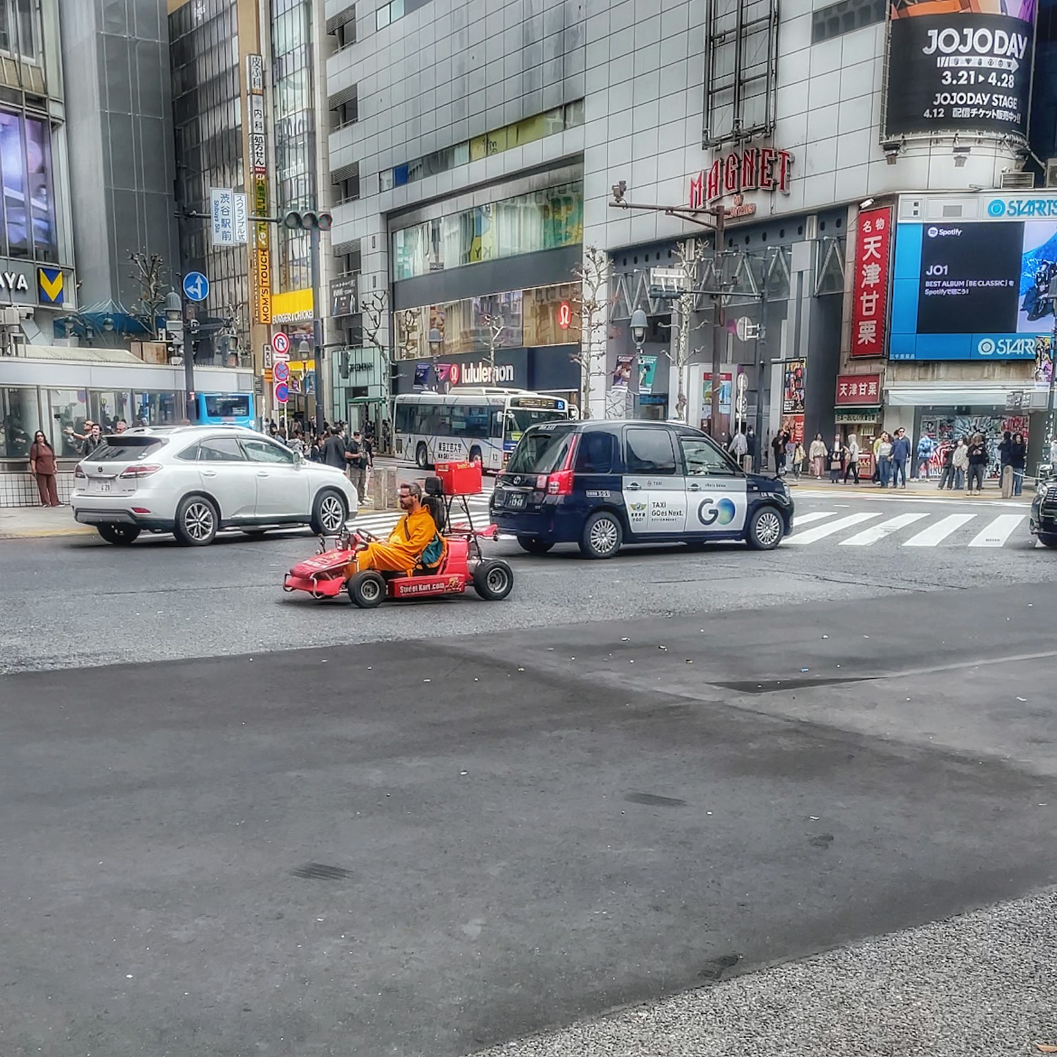 A person driving a go-kart in a busy Tokyo street with cars and advertisements