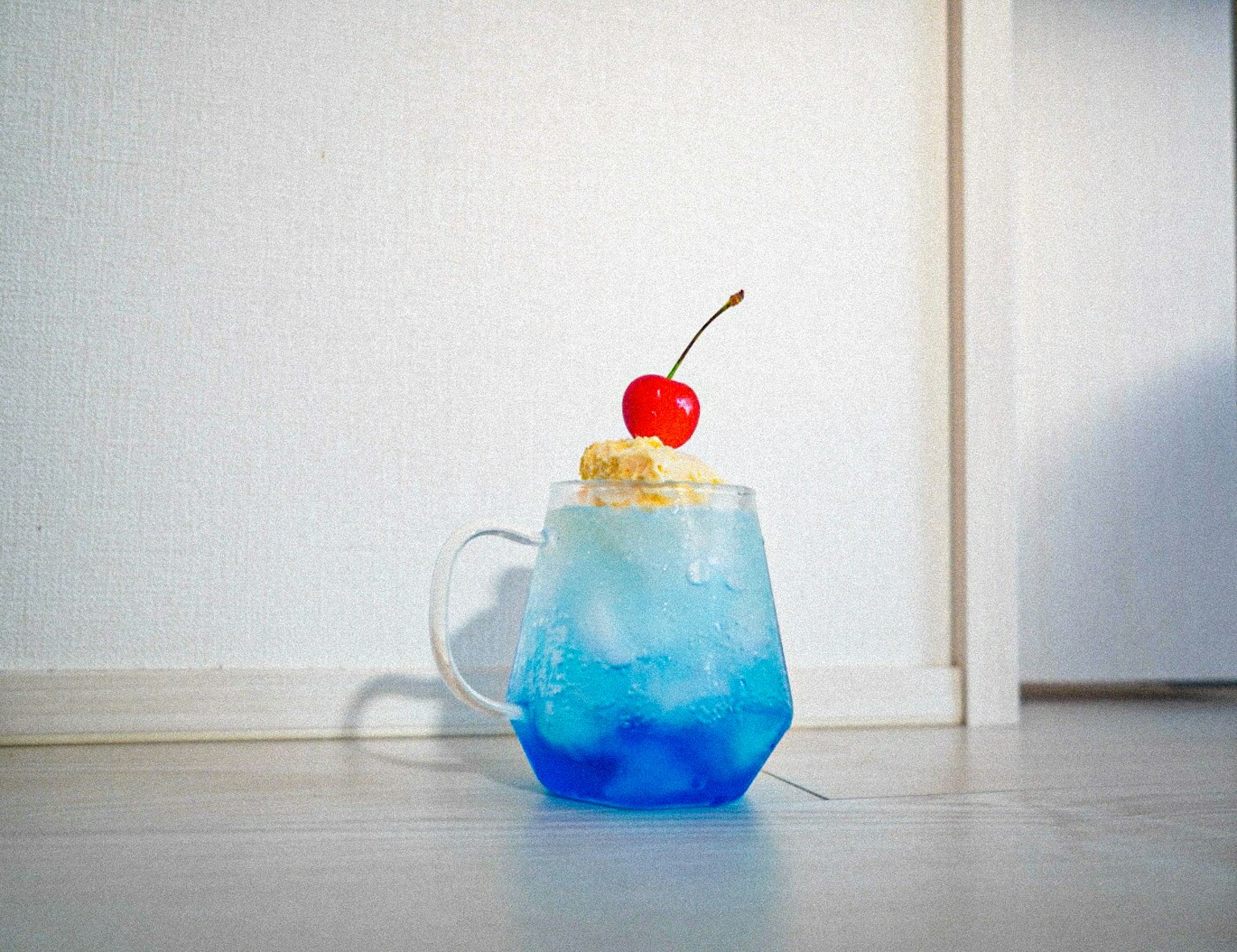 Ein blauer Drink mit Sahne und einer Kirsche in einem Glasbecher