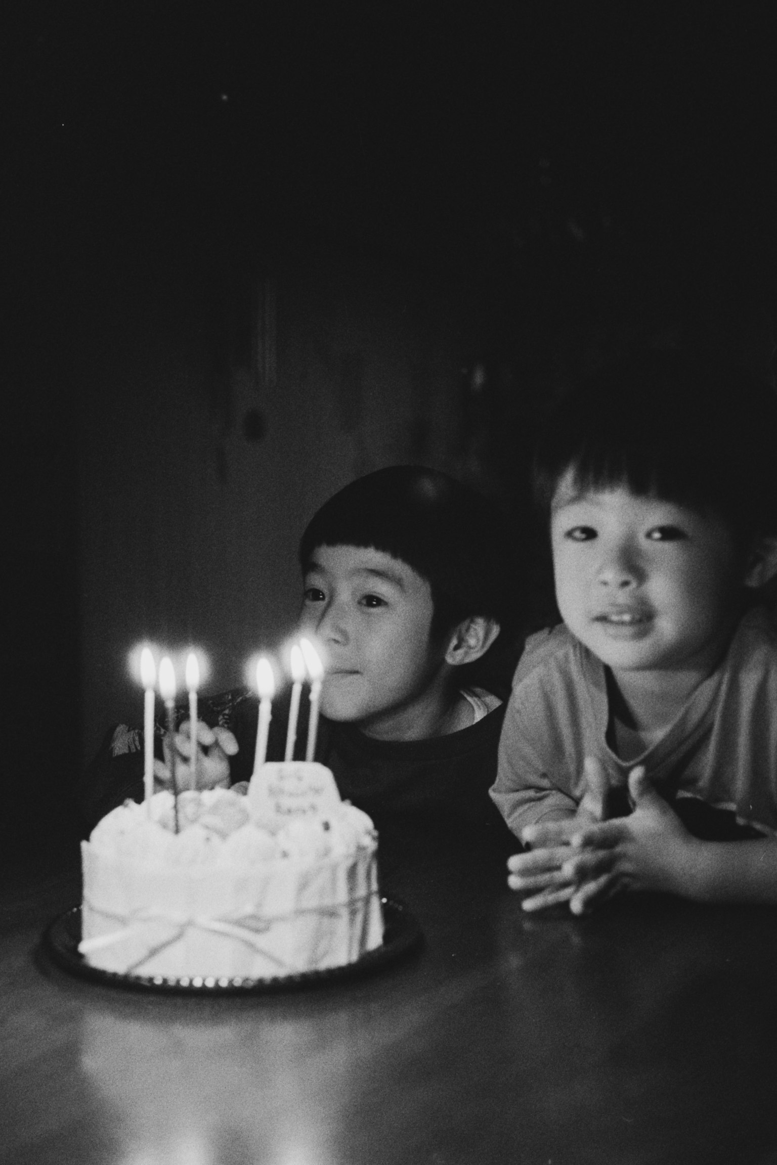 二人の子供が誕生日ケーキの前でキャンドルを見つめているモノクロ写真