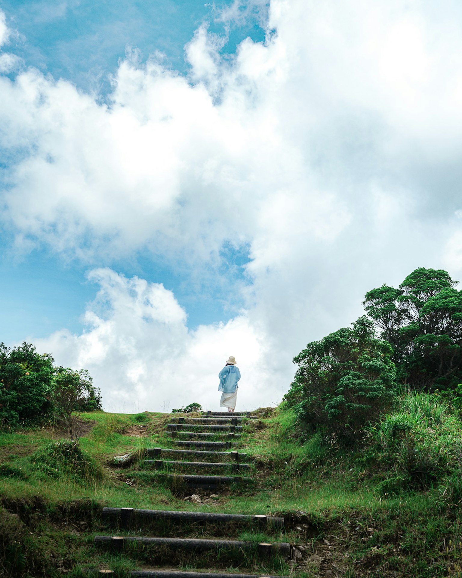 A person walking up stone steps under a blue sky with white clouds