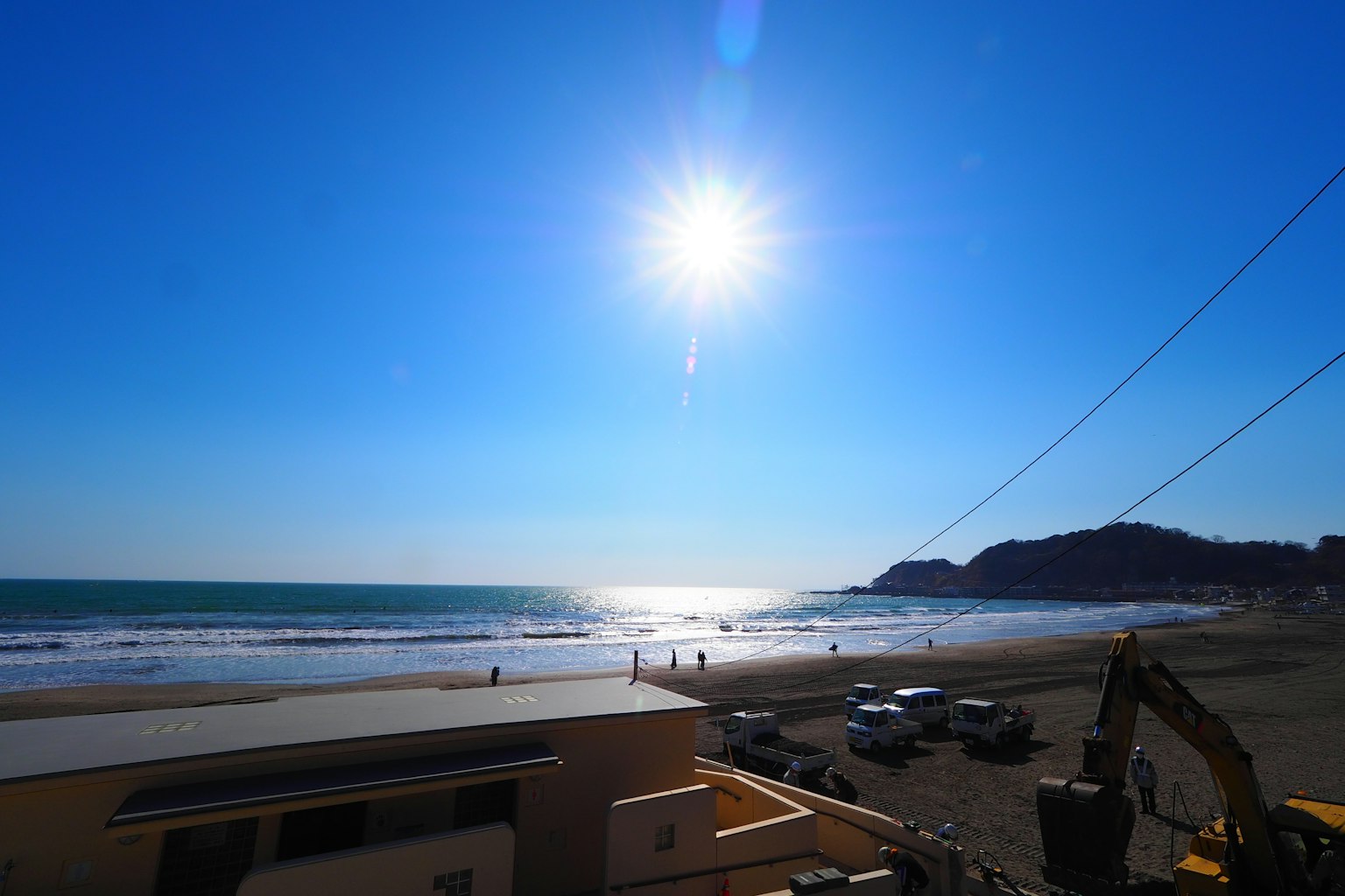 Scena costiera con sole brillante sopra le onde dell'oceano e spiaggia sabbiosa sotto un cielo blu chiaro
