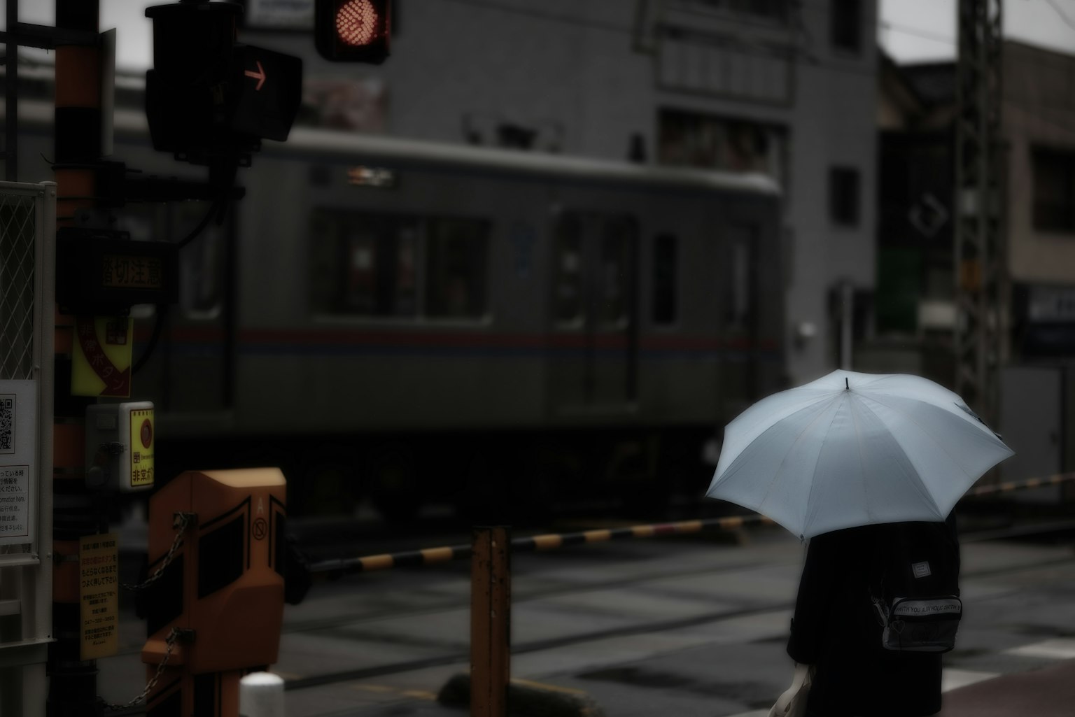Una persona con un paraguas azul esperando en un cruce ferroviario bajo la lluvia
