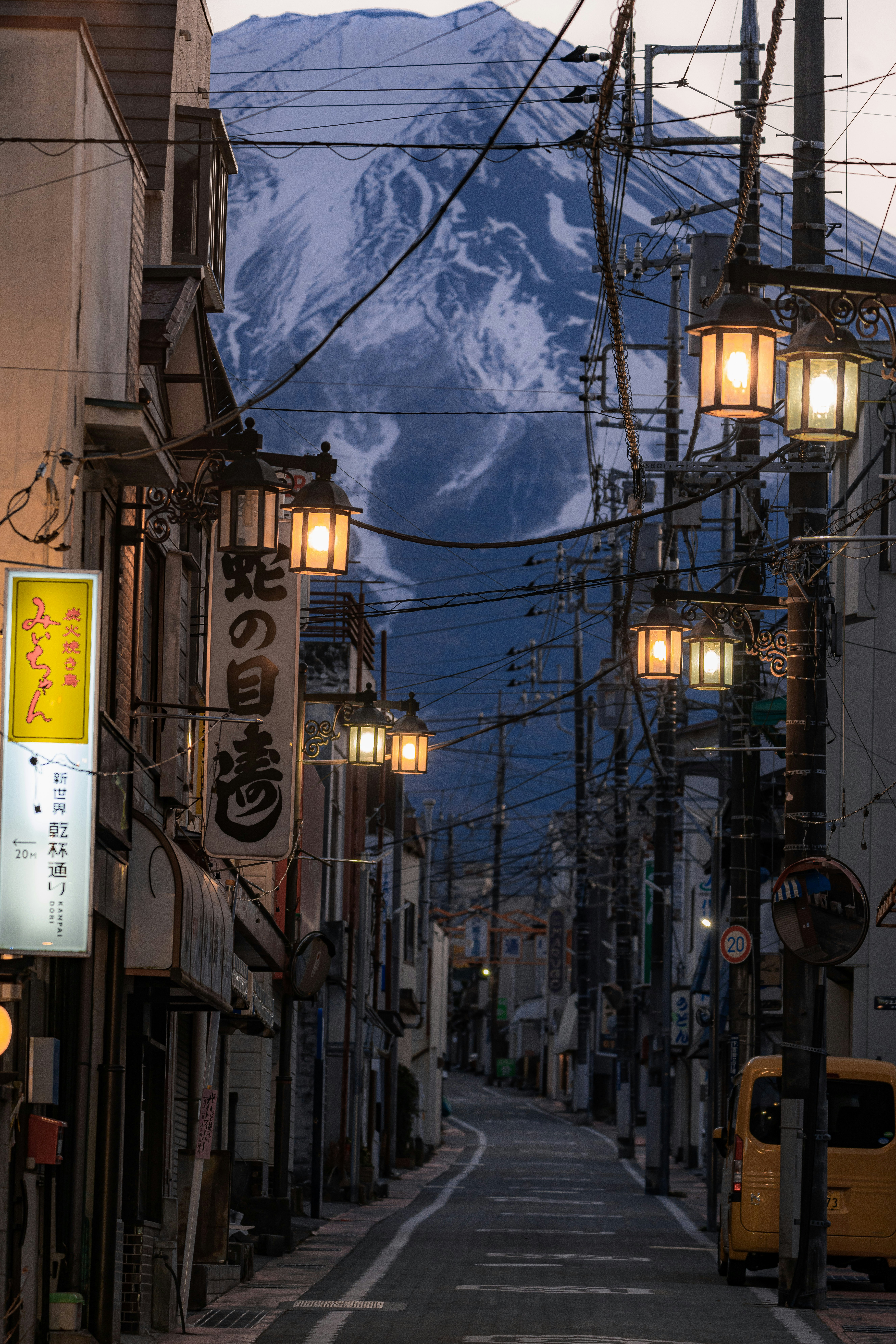 夕暮れの路地に並ぶ提灯と電線のある商店街