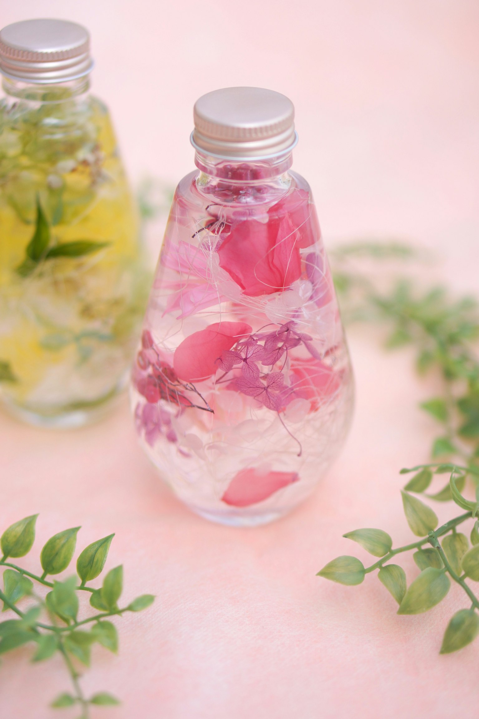 Transparente Flasche mit rosa Blütenblättern und grünen Blättern im Hintergrund