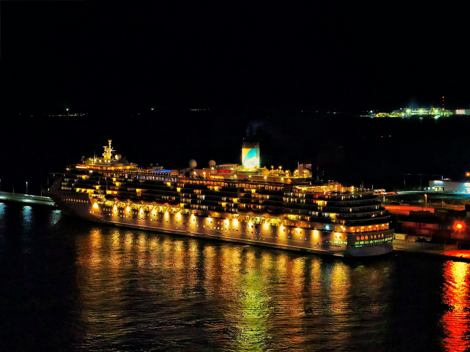 Barco de crucero de lujo atracado de noche con luces reflejándose en el agua