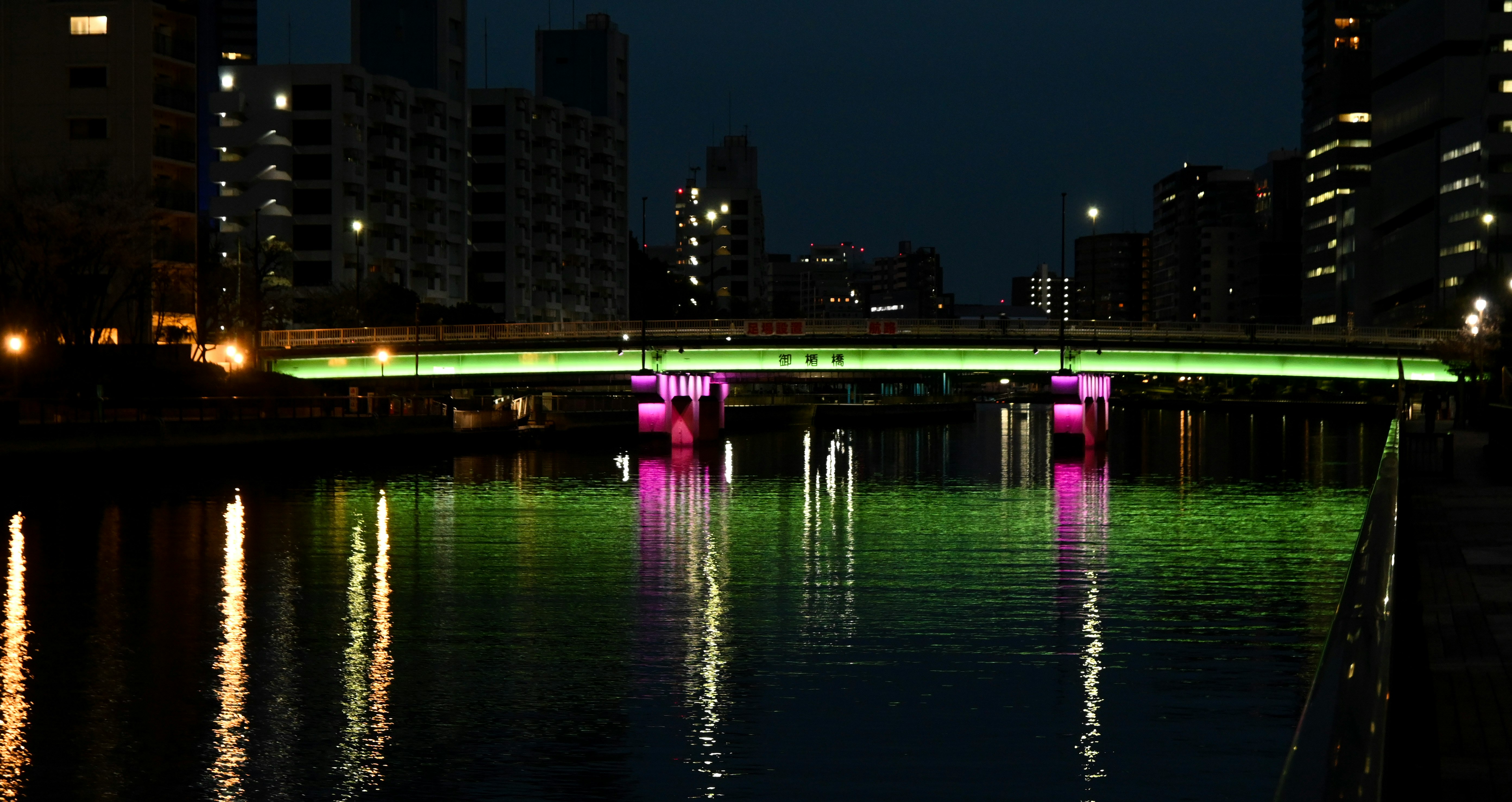 夜の川沿いに映るネオンの橋のライト