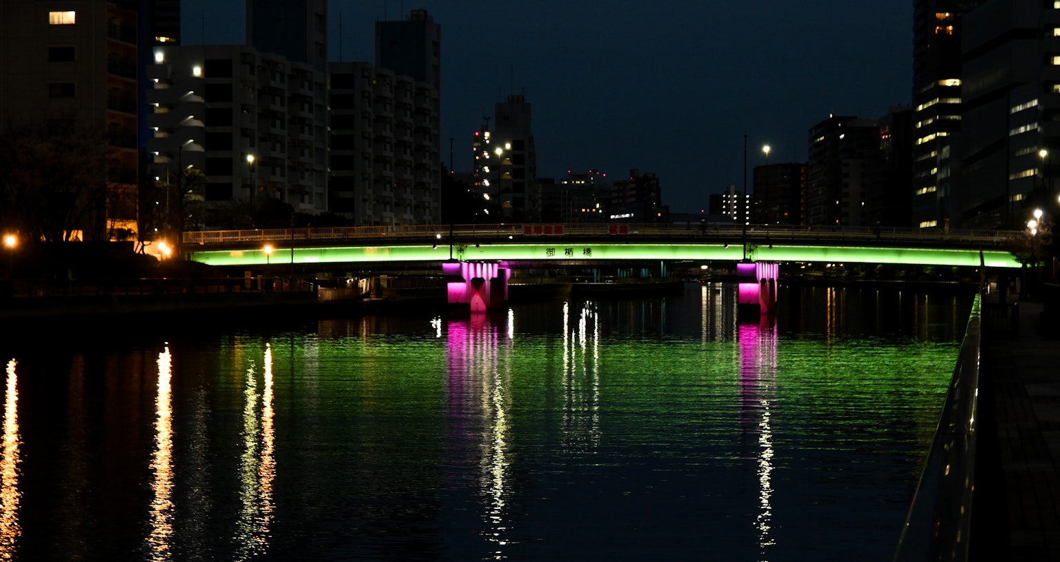 Ponte illuminato con luci verdi e rosa che si riflettono nell'acqua di notte