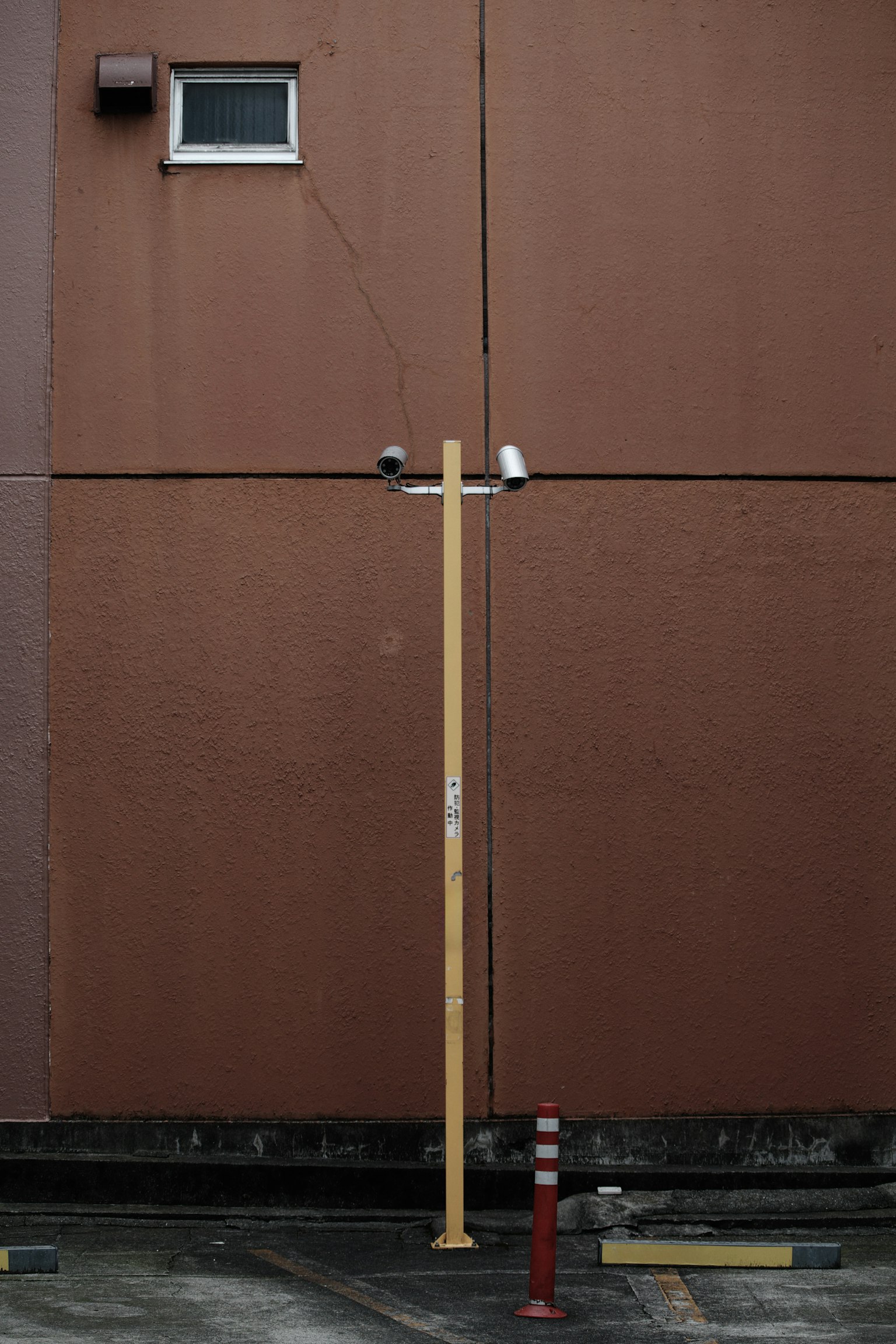 Yellow pole with surveillance cameras against a brown wall