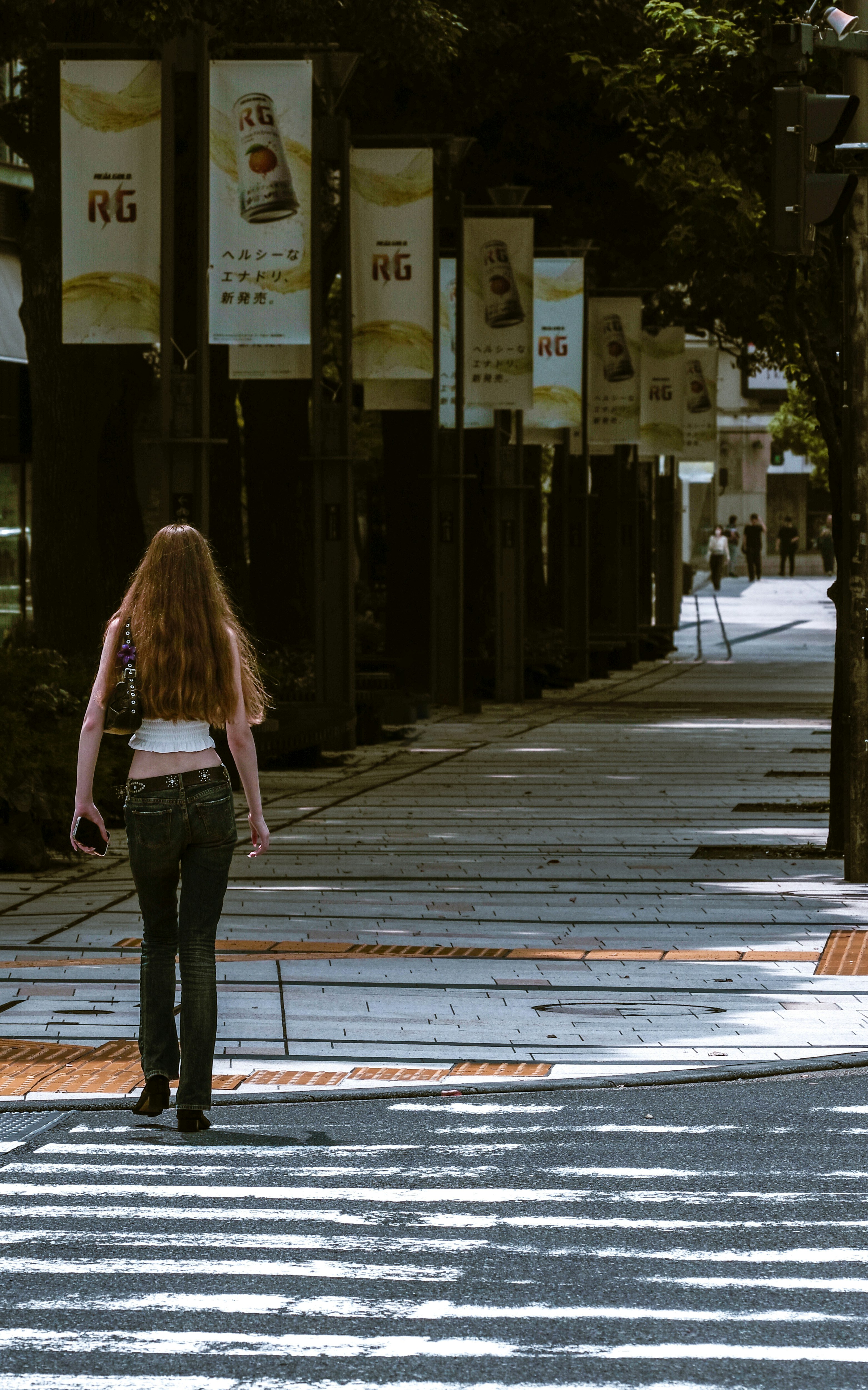 Une personne marche le long d’une rue bordée d’arbres avec un passage piéton