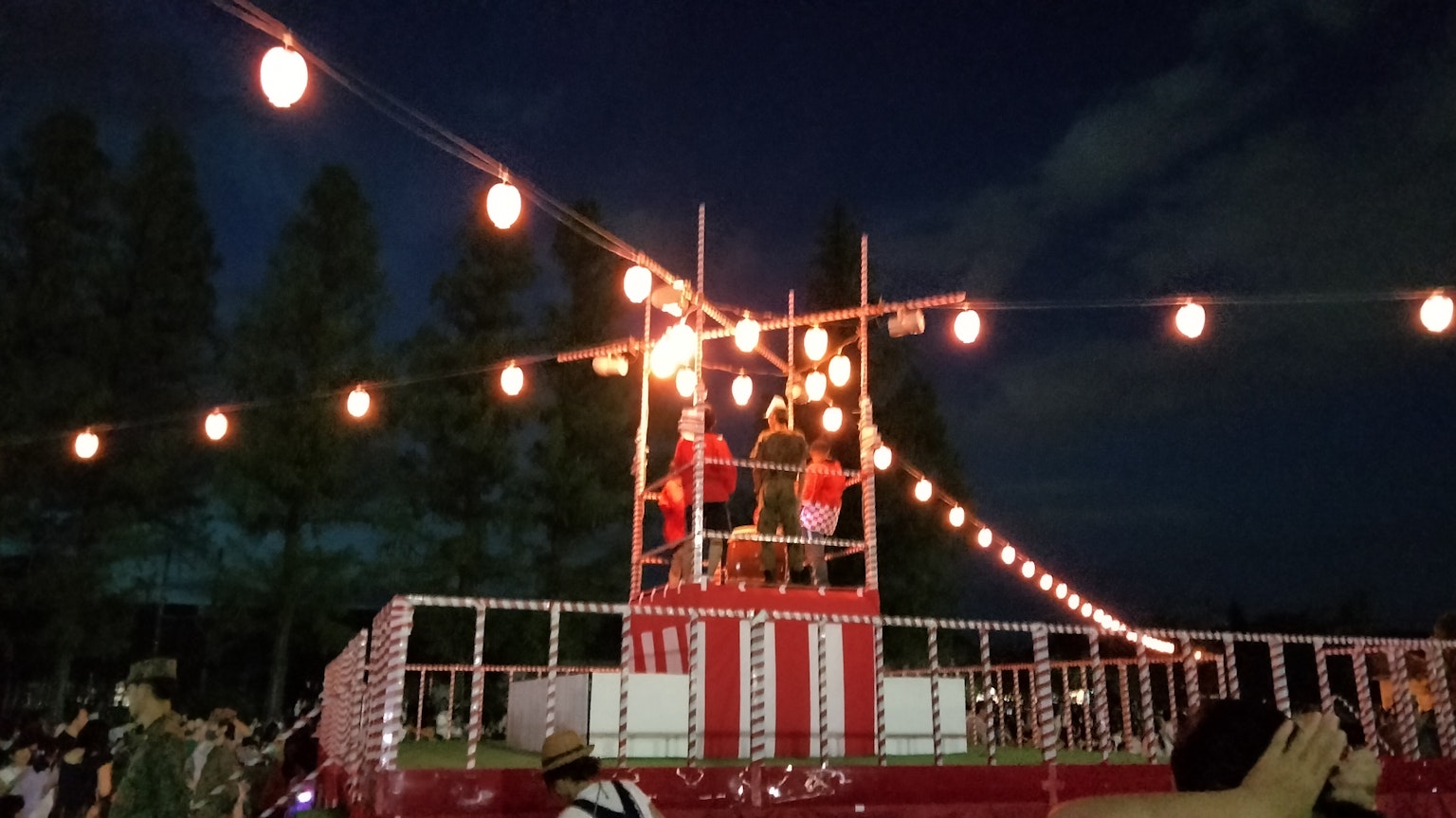 Persone che ballano su un palco rosso illuminato da lanterne durante un festival notturno