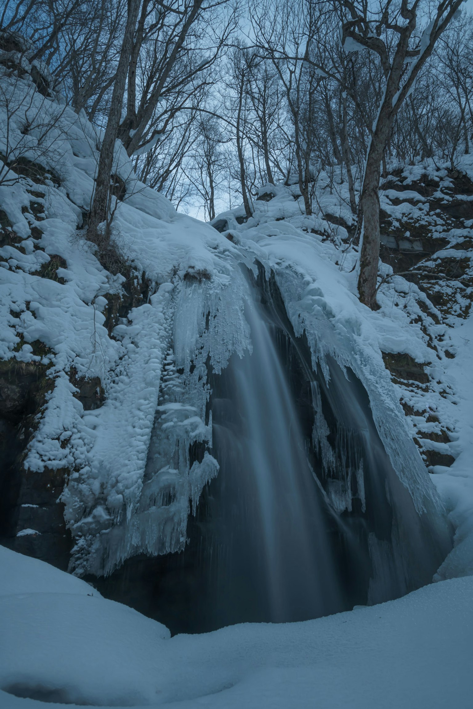 Cascata ghiacciata circondata da neve e formazioni di ghiaccio in un paesaggio invernale